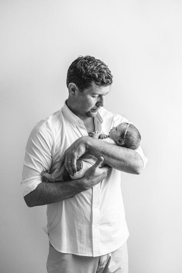  Black an white photo of a dad in a white dress shirt holding his beautiful newborn daughter in his arms. #nicolehawkinsphotography #secondchild #chatham #newjersey #inhomephotography #nicolehawkinsnewborns #newbornsession #njfamilyphotographer 