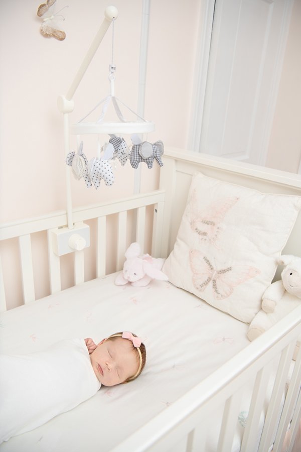  Newborn baby girl sleeping swaddled in a white crib with neutral baby toys in a blush pink nursery. #inhomephotography #babynursery #nicolehawkinsphotography #chatham #newjersey #nicolehawkinsnewborns #newbornsession #njfamilyphotographer 