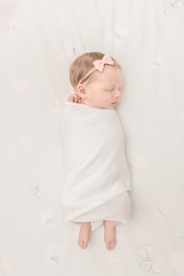  Beautiful newborn baby girl in a pink bow wrapped in a white swaddle with her toes peeking out. newborn poses #newbornportraits #njfamilyphotographer #newjersey #nicolehawkinsnewborns #chatham #inhomephotography #babynursery #niolehawkinsphotography