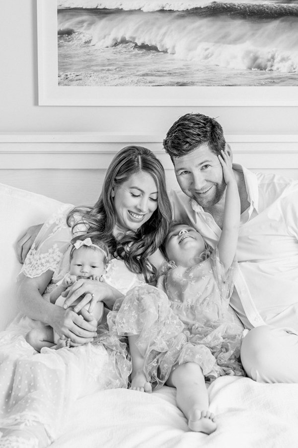  Black and white family portrait of two sisters cuddled on a bed with mom and dad in their home. #newbornfamilyportraits #familyoffour #nicolehawkinsphotography #inhomephotography #njfamilyphotographer #chatham #newjersey #nicolehawkinsnewborns 