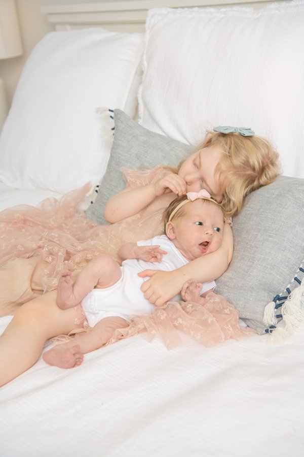  Sweet photo of big sister in a pink tulle dress cuddling with her newborn baby sister on the bed. #nicolehawkinsnewborns #njfamilyphotographer #chatham #newjersey #newbornfamilyportraits #nicolehawkinsphotography #inhomeportraits #secondtimeparents 