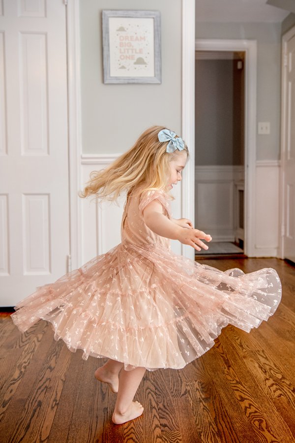  Toddler girl with long blonde hair twirling in her sparkly pink dress in the living room of her New Jersey home. #toddlerfashion #inhomeportraits #chatham #newjersery #njfamilyphotographer #bigsister #familyportraits #nicolehawkinsphotography 
