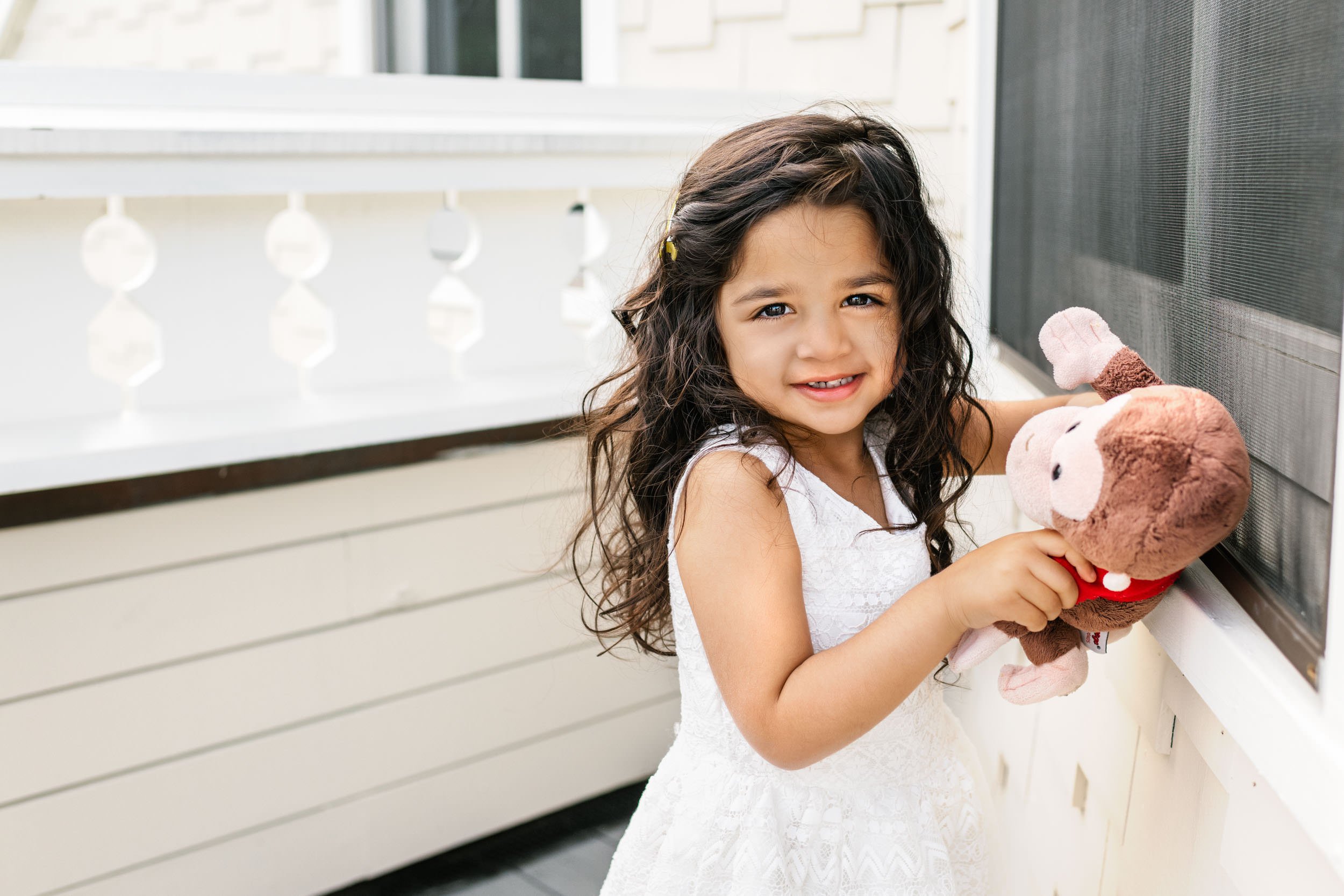  Toddler Indian girl with long and curly dark hair plays with her stuffed animal on the front porch #newjersyphotographers #njfamilyphotoographer #toddler #nicolehawkinsphotography #inhomeportraits #nicolehawkinsfamilies #glenridge #newjersey #funpos