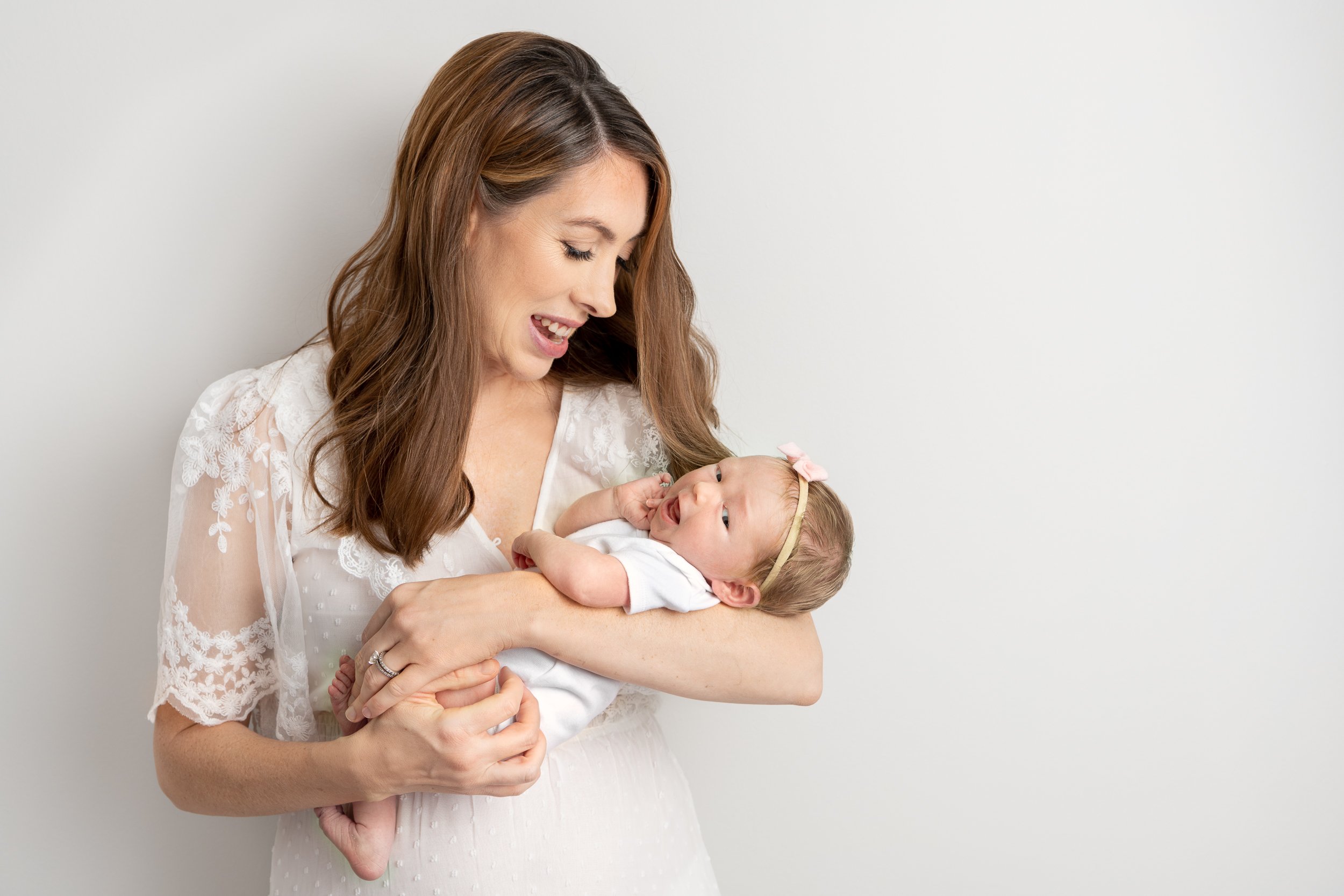  Precious baby girl smiles while her mom holds her and smiles lovingly in a lace dress. #motherdaughter #newbornportraits #inhomephotography #babynursery #nicolehawkinsphotography #chatham #newjersey #njfamilyphotographer #nicolehawkinsnewborns 