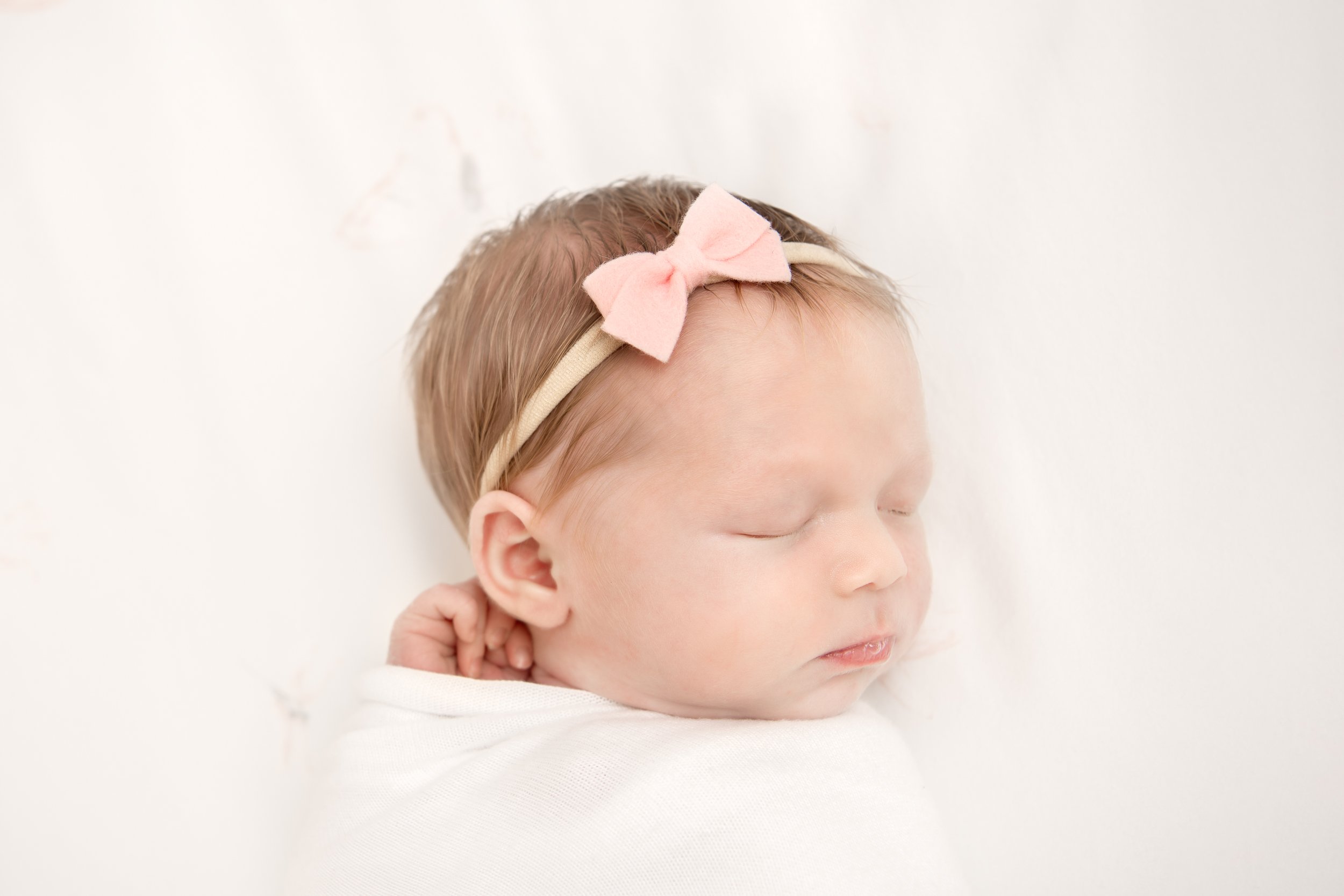  Newborn baby girl wearing a pink bow headband lying in her crib while swaddled. #inhomeportraits #motherdaughter #nicolehawkinsphotography #chatham #newjersey #njfamilyphotographer #nicolehawkinsphotography #inhomenewbornportraitsession #newborndeta