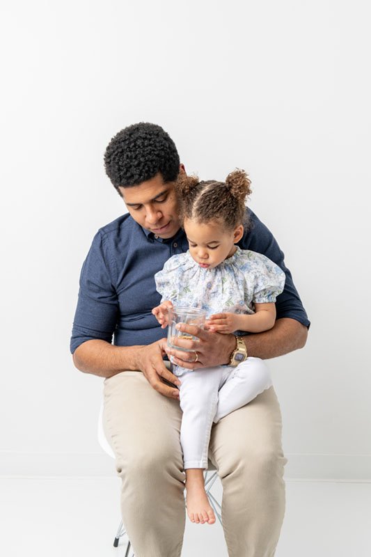  In a New Jersey studio, a father is captured holding his little girl with pigtails on his lap by Nicole Hawkins Photography. daddy daughter pic #NicoleHawkinsPhotography #NicoleHawkinsBabies #StudioPhotography #NewJerseyPhotographer #twinphotography