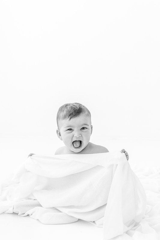  Portrait of a sixth-month-old baby playing with a white sheet smiling by Nicole Hawkins Photography. baby playing photography session #sixmonthbabyportraits #NJPhotographer #NicoleHawkinsPhotography #NicoleHawkinsBabies #BabyStudioPhotography    