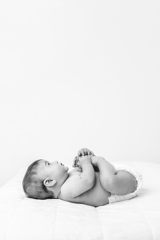 Nicole Hawkins Photography captures a simple classy portrait of a child laying on a bed in a white studio. black white child portrait #sixmonthbabyportraits #NJPhotographer #NicoleHawkinsPhotography #NicoleHawkinsBabies #BabyStudioPhotography    