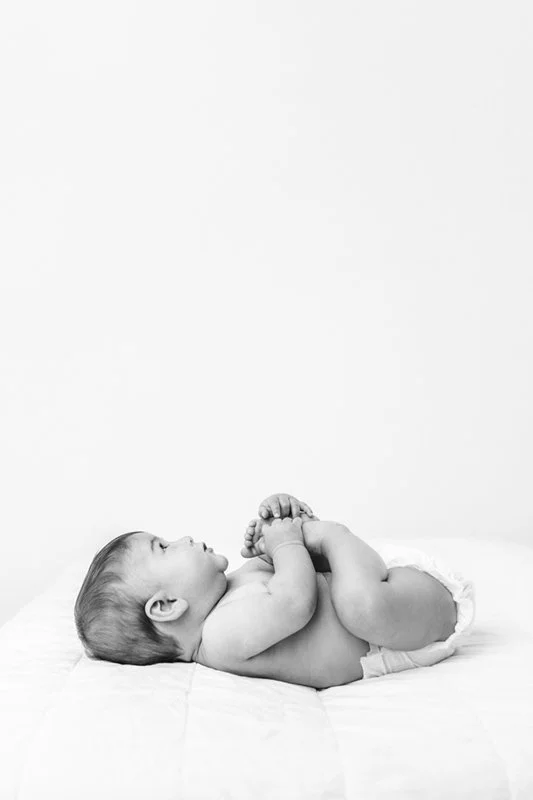  Nicole Hawkins Photography captures a simple classy portrait of a child laying on a bed in a white studio. black white child portrait #sixmonthbabyportraits #NJPhotographer #NicoleHawkinsPhotography #NicoleHawkinsBabies #BabyStudioPhotography    