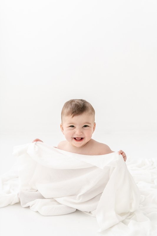  All white studio child portrait with 6-month-old baby playing by Nicole Hawkins Photography. all white baby pic inspiration NJ #sixmonthbabyportraits #NJPhotographer #NicoleHawkinsPhotography #NicoleHawkinsBabies #BabyStudioPhotography    