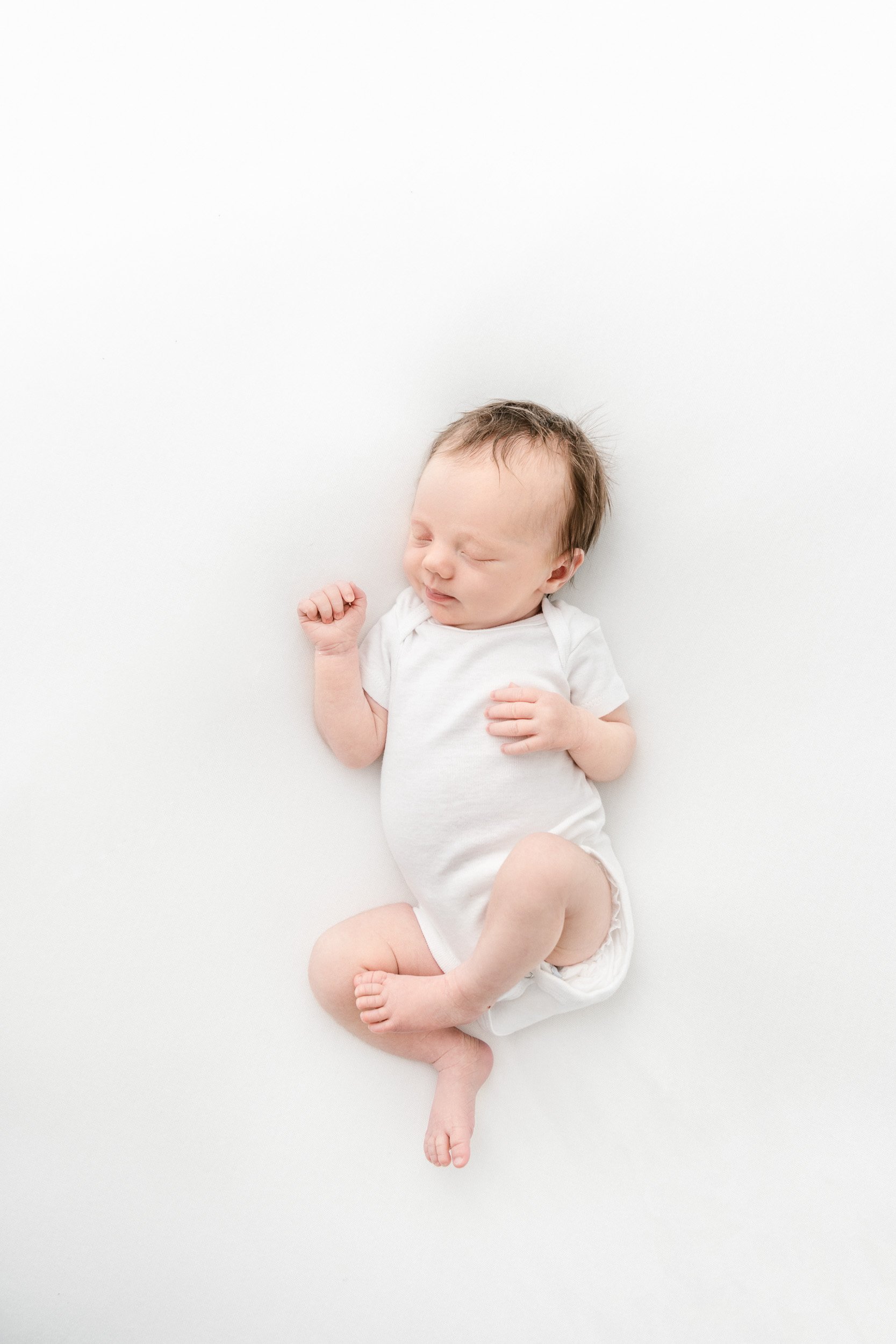  A little girl in a white onesie sleeping during a newborn session with Nicole Hawkins Photography in New Jersey. simple newborns #NicoleHawkinsPhotography #NicoleHawkinsNewborns #StudioPhotography #NewYorkPhotographer #NJphotographers #newborn 