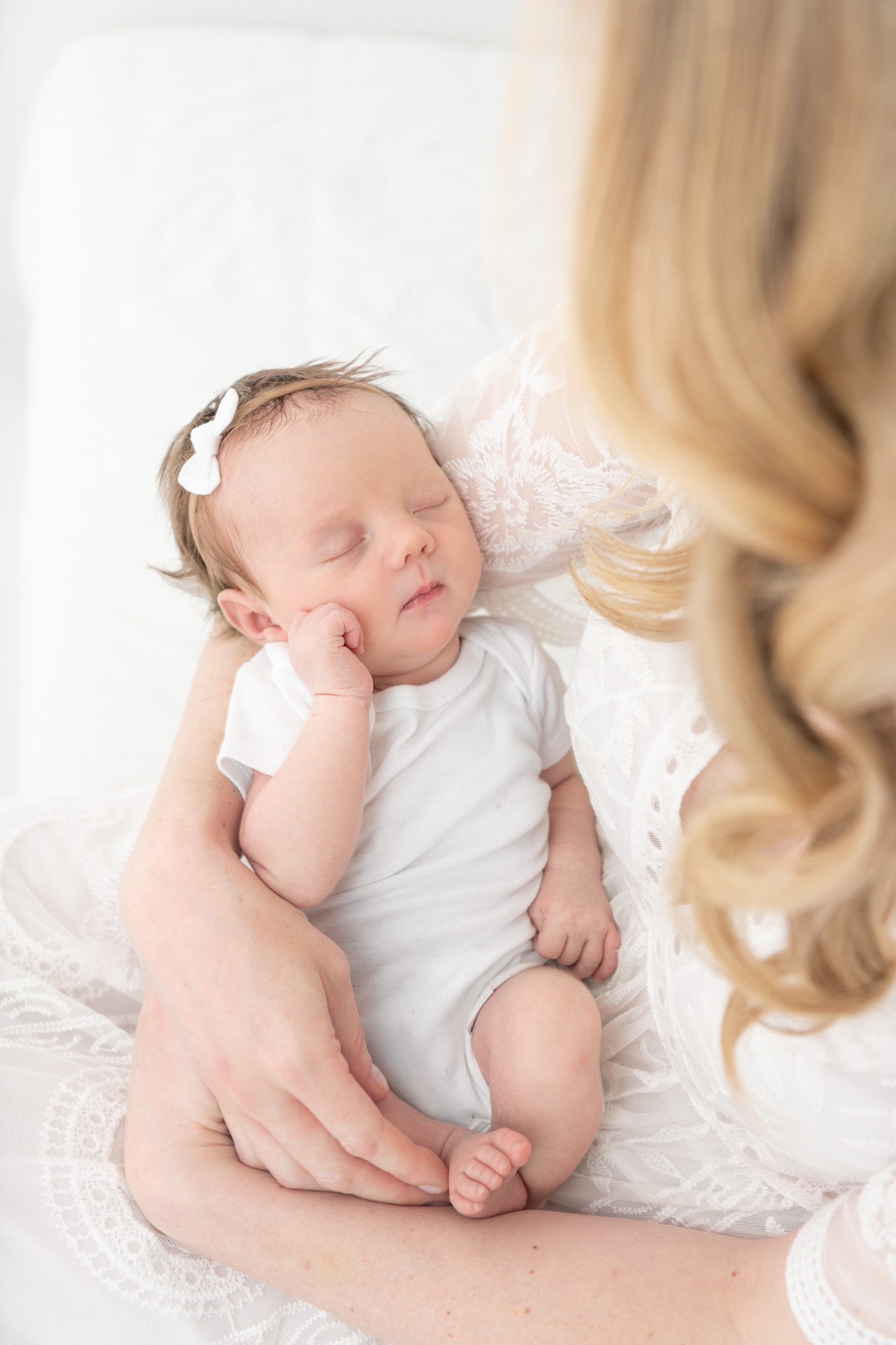  A newborn baby girl is held in her mother's arms in a white studio by Nicole Hawkins Photography. baby girl all in white #NicoleHawkinsPhotography #NicoleHawkinsNewborns #StudioPhotography #NewYorkPhotographer #NJphotographers #newborn 