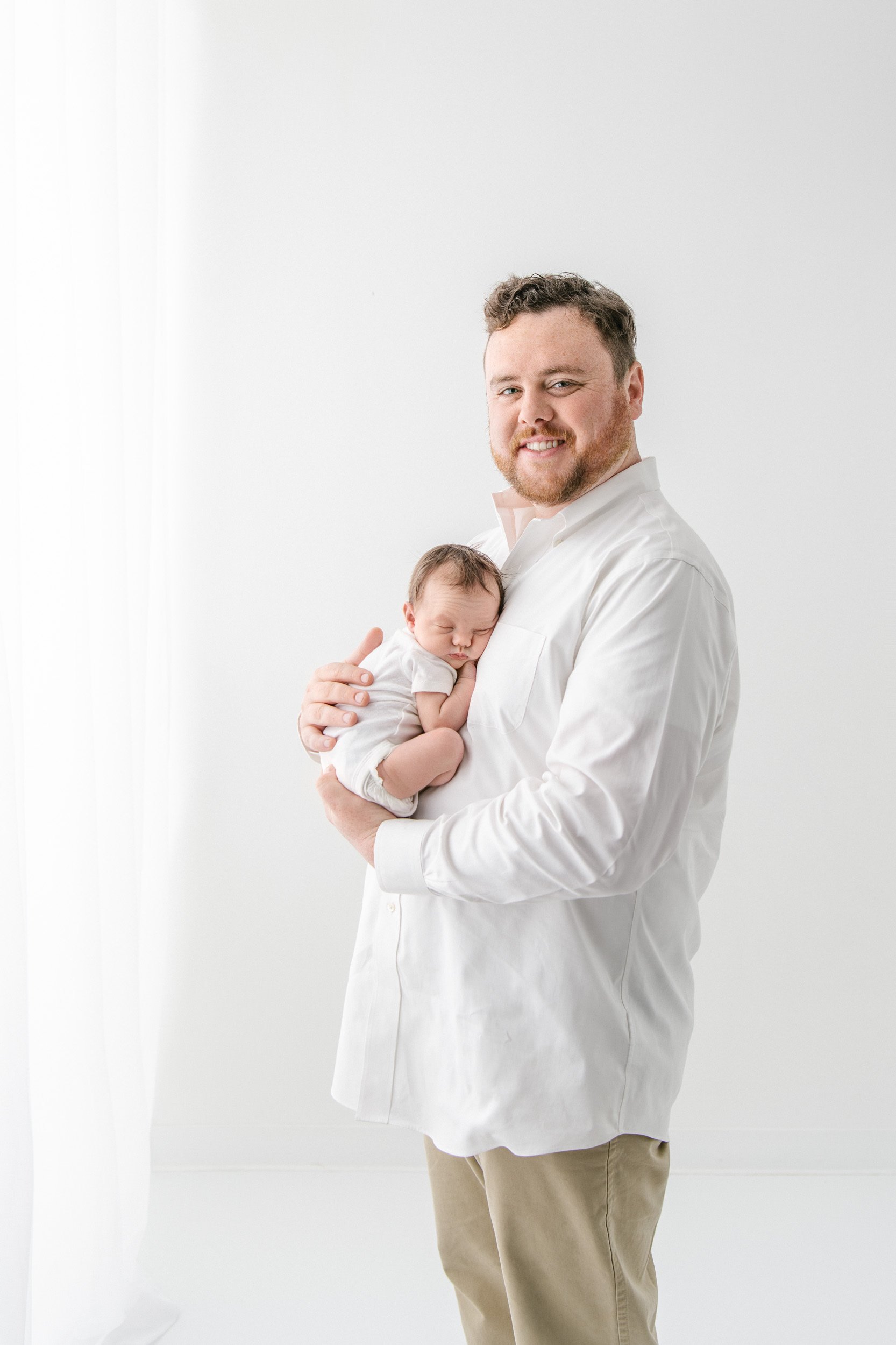  A father holds his baby girl in his arms as he smiles captured by Nicole Hawkins Photography. studio newborn photography NJ #NicoleHawkinsPhotography #NicoleHawkinsNewborns #StudioPhotography #NewYorkPhotographer #NJphotographers #newborn 