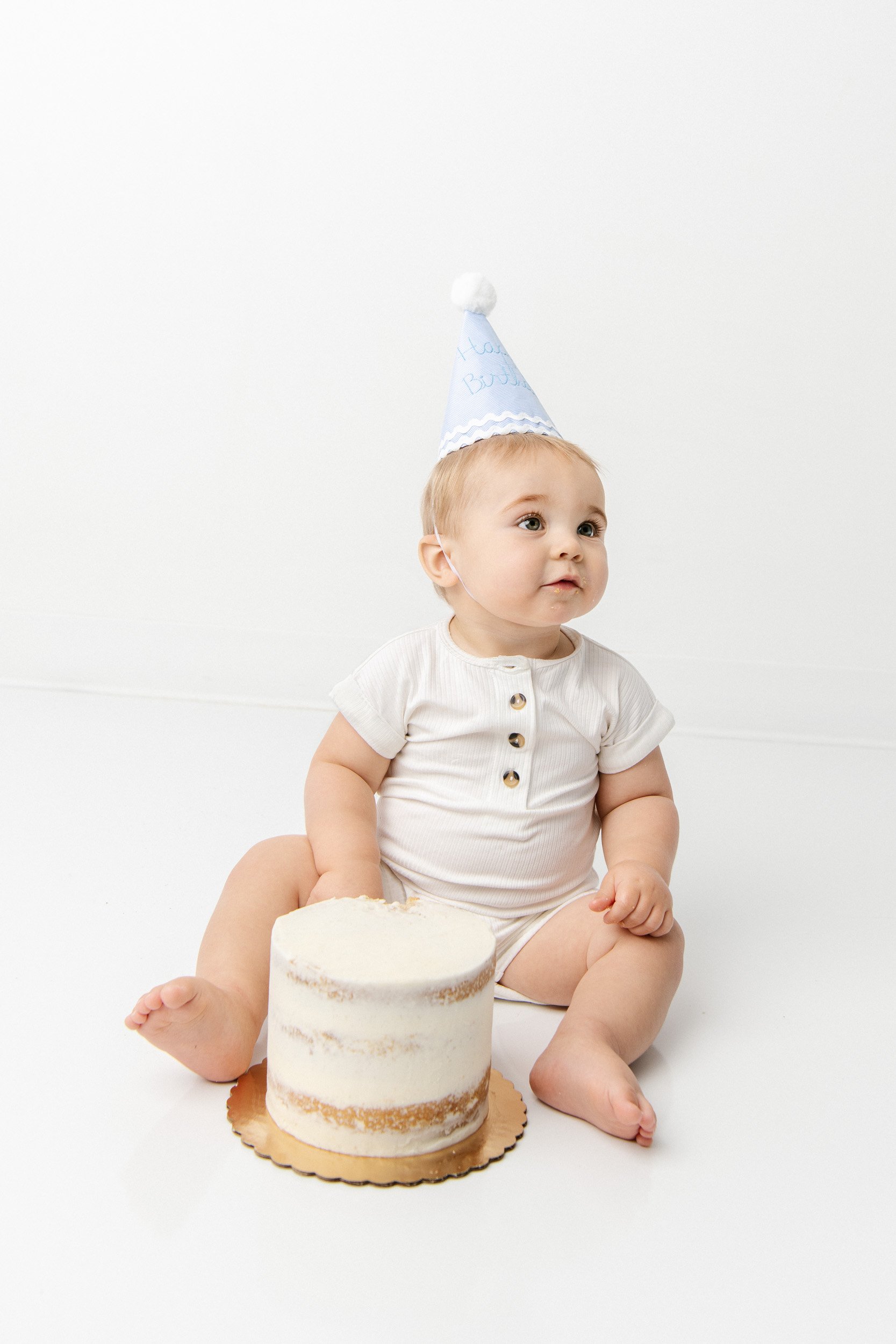  Baby with his first birthday cake wearing a party hat in a studio by Nicole Hawkins Photography. party hat cake #NicoleHawkinsPhotography #NicoleHawkinsBabies #BirthdayStudioPhotography #smashcake #firstbirthday #studiobabiesandchildren 