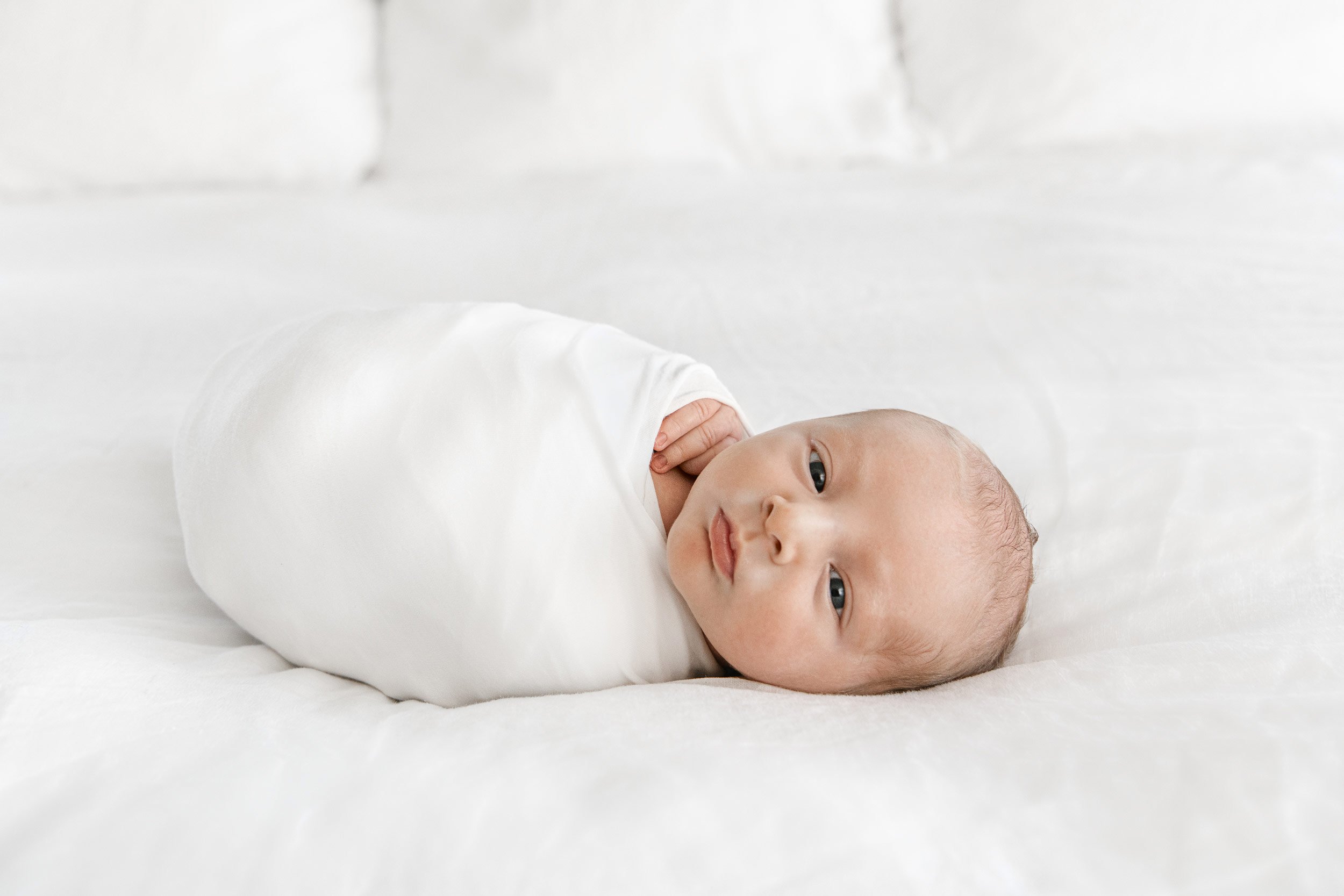  Nicole Hawkins Photography an NJ newborn Photographer captures a baby on a bed in a white swaddle. in home newborn pics #NicoleHawkinsPhotography #InHomeNewborn #JerseyShoreNewborn #MontclairPhotographers #NewbornPhotography #baby #newborn 