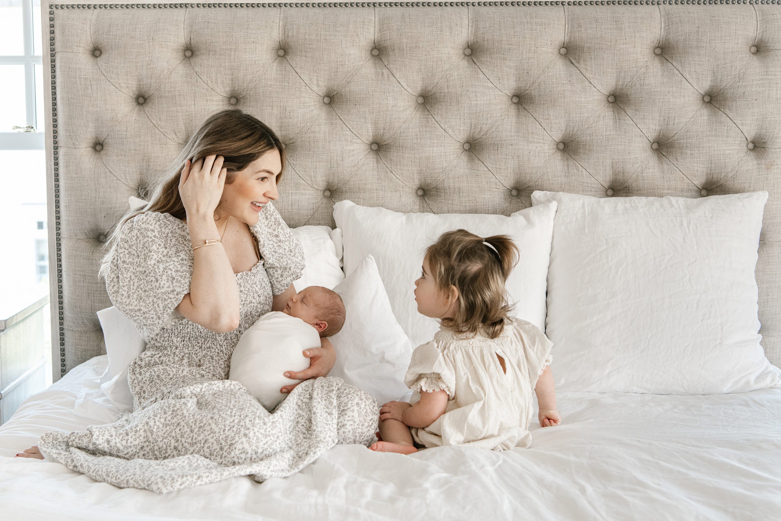  A mother sits on her bed with her newborn and toddler little girl by Nicole Hawkins Photography. NJ photographer #NicoleHawkinsPhotography #InHomeNewborn #JerseyShoreNewborns #MontclairPhotographers #NewbornPhotography #baby #newborn 