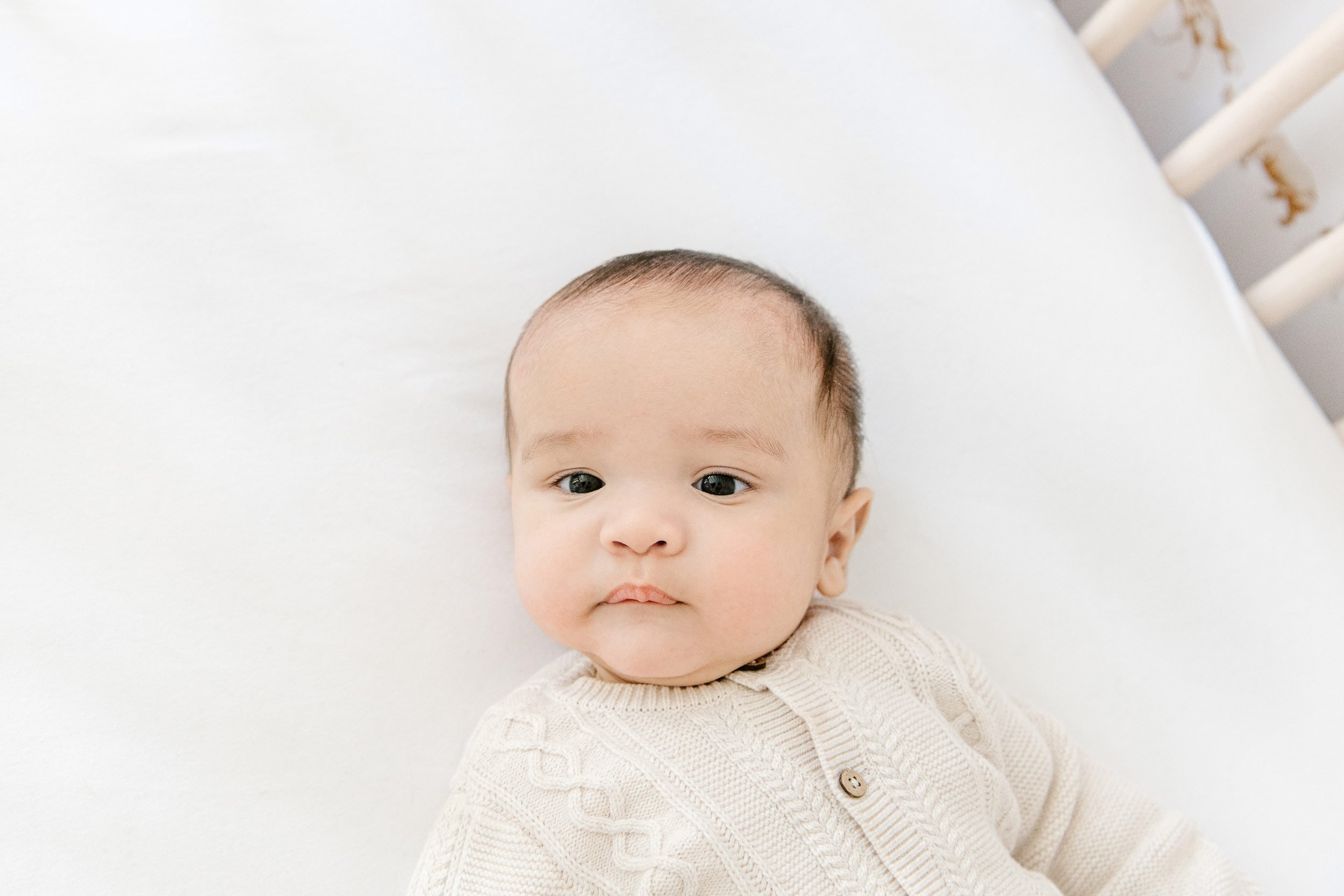  Nicole Hawkins Photography captures a baby boy in a cream sweater lying in his crib. In-home baby photography baby boy #NicoleHawkinsPhotography #InHomeNewborns #NurseryNewborns #NYCbabyphotography #babyportraits #ZooNursery #familyportraits 