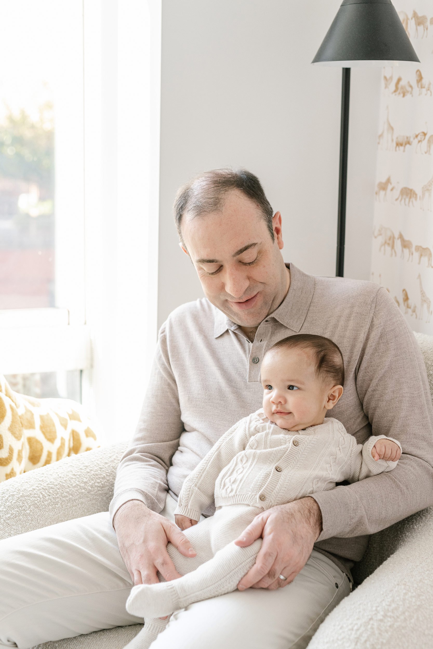  A father holding his baby boy and playing with him captured by Nicole Hawkins Photography. father with his baby boy daddy's boy #NicoleHawkinsPhotography #InHomeNewborns #NurseryNewborns #NYCbabyphotography #babyportraits #ZooNursery #familyportrait