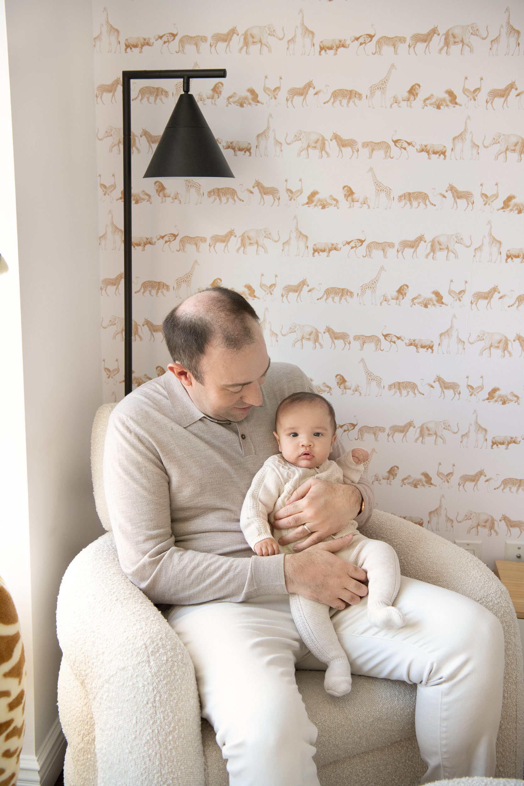  A father sits in a lounge chair in the baby nursery holding his son by Nicole Hawkins Photography. safari nursery #NicoleHawkinsPhotography #InHomeNewborns #NurseryNewborns #NYCbabyphotography #babyportraits #ZooNursery #familyportraits 