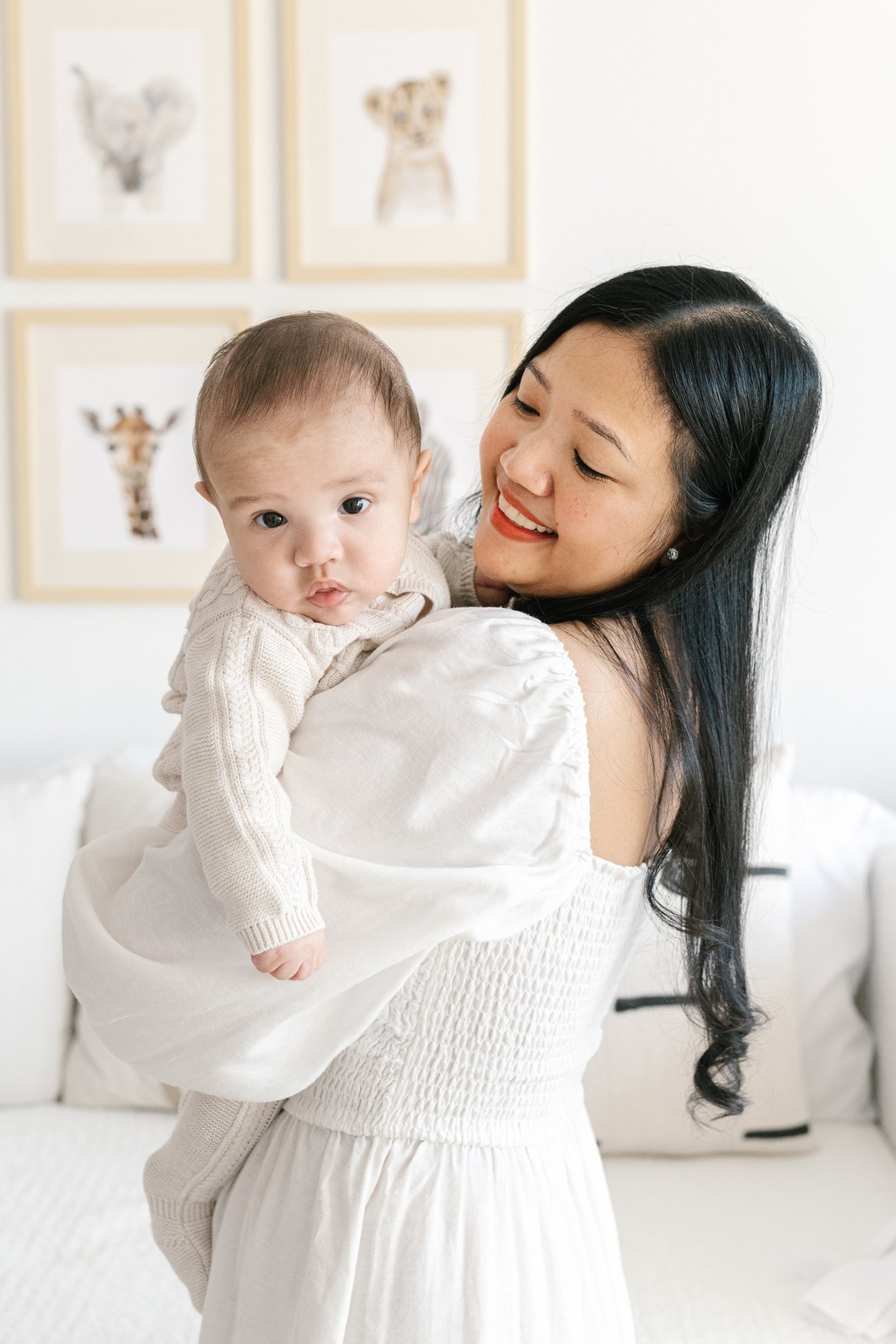  A mother holds her baby in front of framed animal prints by Nicole Hawkins Photography. beautiful nursery #NicoleHawkinsPhotography #InHomeNewborns #NurseryNewborns #NYCbabyphotography #babyportraits #ZooNursery #familyportraits 