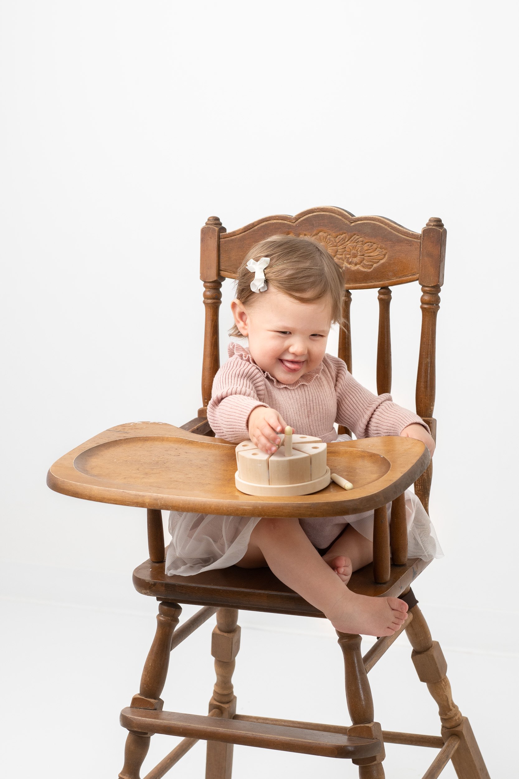  Sitting in an antique high chair a baby girl reaches for her birthday cake by Nicole Hawkins Photography. high chair cake smash #NicoleHawkinsPhotography #NicoleHawkinsBabies #studiochildren #firstbirthday #studiophotography #girlsbirthdayportraits 