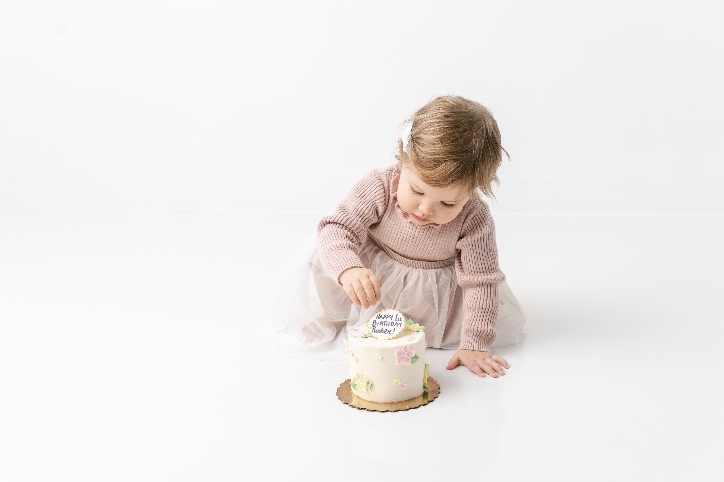 Nicole Hawkins Photography captures a baby girl touching her first birthday cake with buttercream flowers. floral birthday cake #NicoleHawkinsPhotography #NicoleHawkinsBabies #studiochildren #firstbirthday #studiophotography #girlsbirthdayportraits 