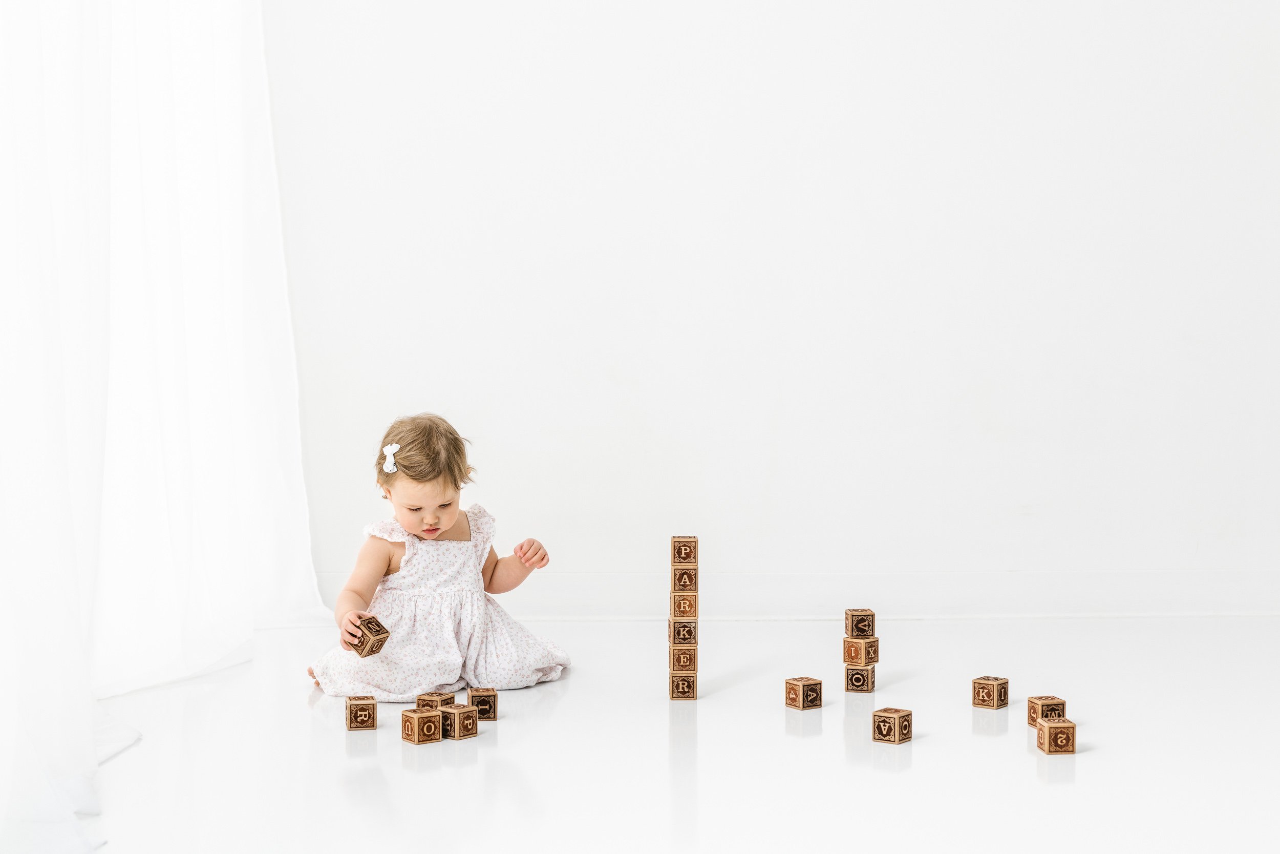  During a first birthday session, a little girl stacks wooden blocks by Nicole Hawkins Photography. wooden blocks photography #NicoleHawkinsPhotography #NicoleHawkinsBabies #studiochildren #firstbirthday #studiophotography #girlsbirthdayportraits 