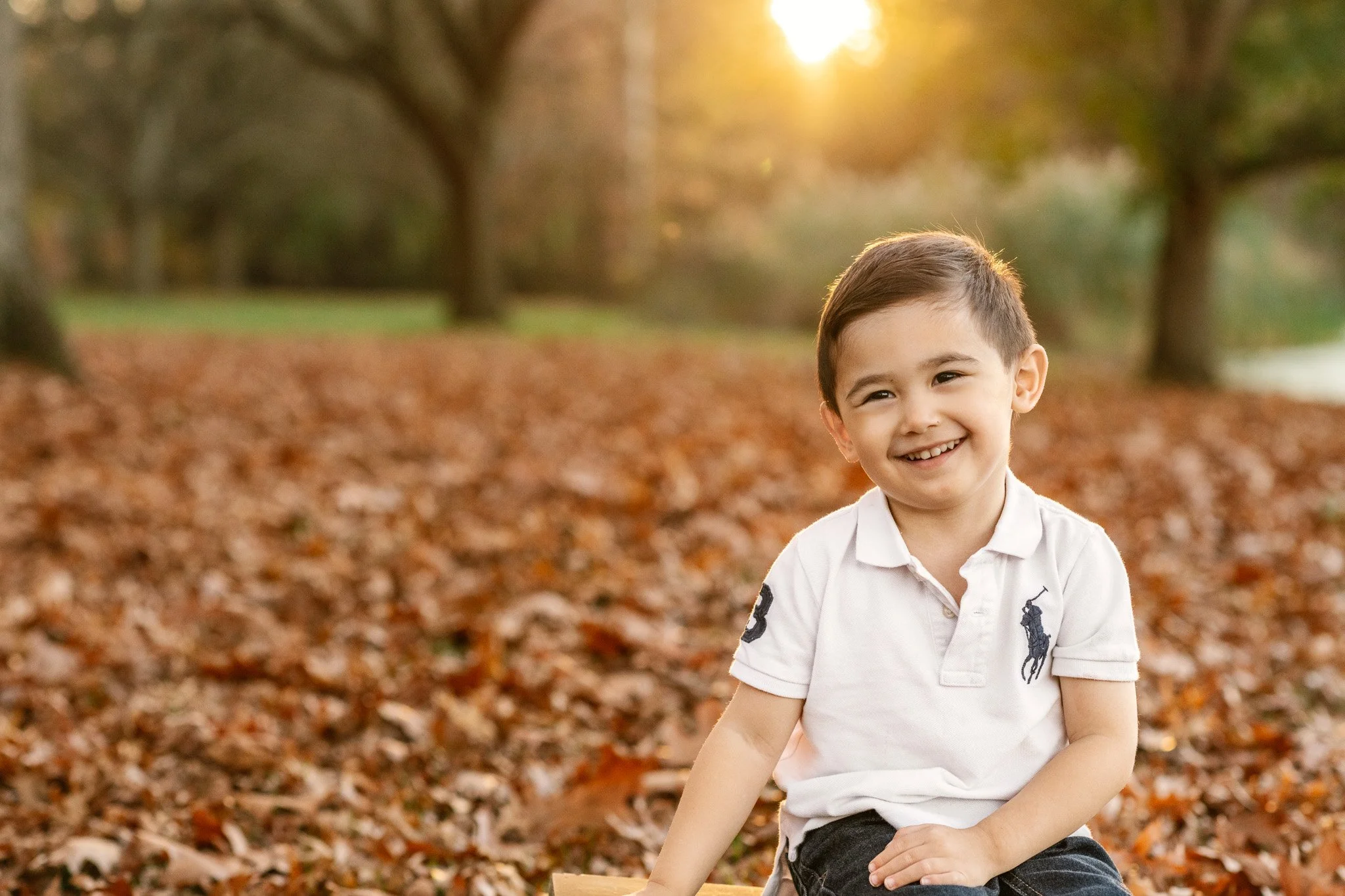  A little boy sitting in a pile of leaves with the sun setting behind him by Nicole Hawkins Photography. fall outdoor portraits #NicoleHawkinsPhotography #NicoleHawkinsFamilies #fallfamilyphotos #NorthernNewJerseyPhotography #outdoorfamilyportraits 