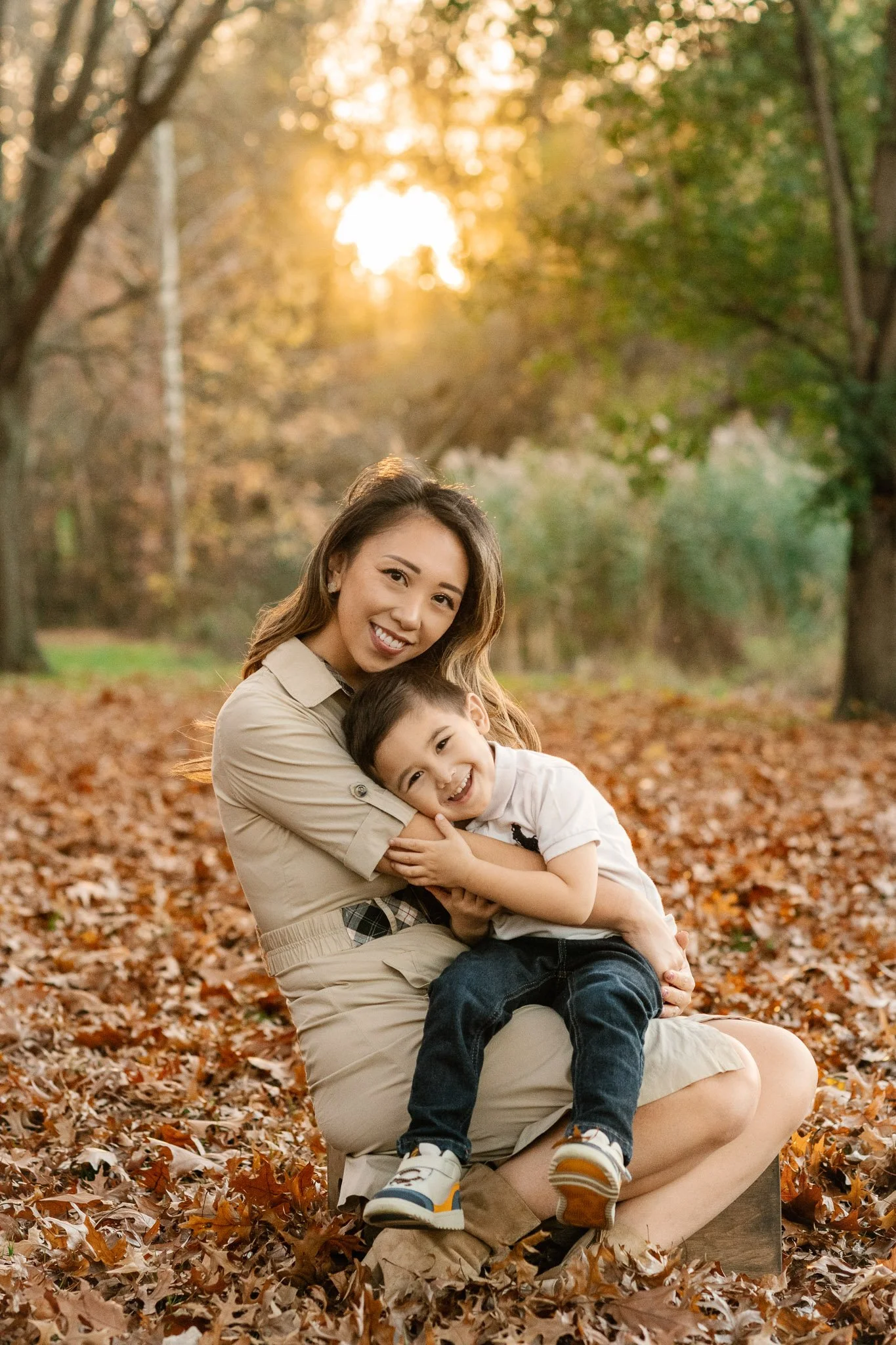  With a sunburst behind her, a mother snuggles her little boy sitting in a pile of leaves by Nicole Hawkins Photography. fall #NicoleHawkinsPhotography #NicoleHawkinsFamilies #fallfamilyphotos #NorthernNewJerseyPhotography #outdoorfamilyportraits 