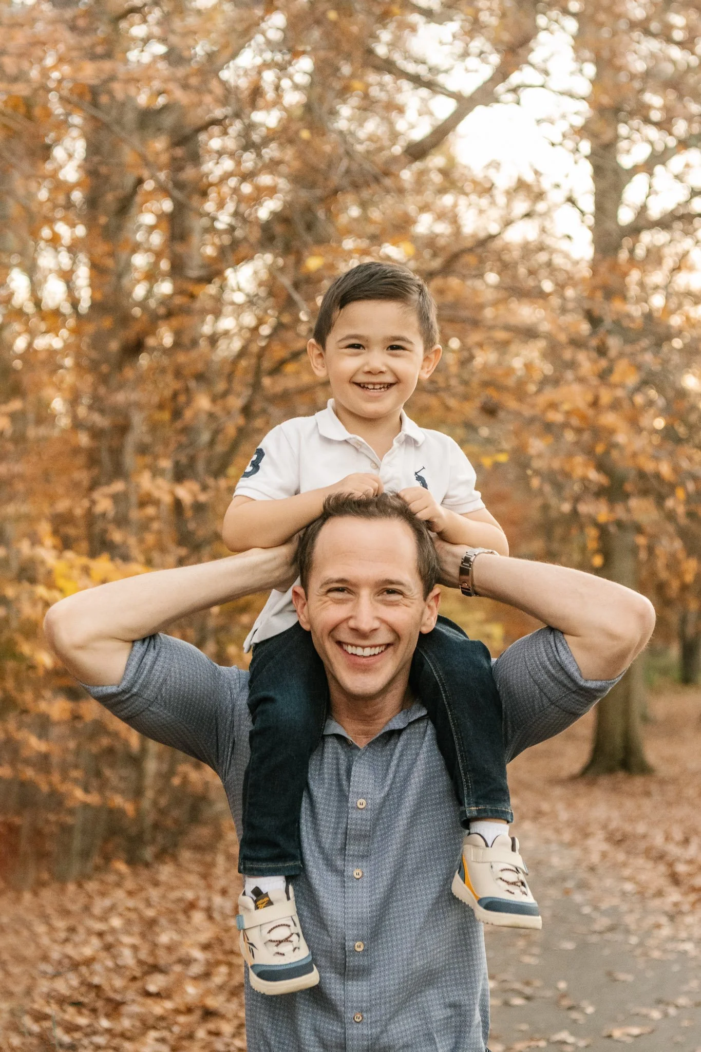  A little boy sits on his father's shoulders by Nicole Hawkins Photography during autumn in New Jersey. father with son #NicoleHawkinsPhotography #NicoleHawkinsFamilies #fallfamilyphotos #NorthernNewJerseyPhotography #outdoorfamilyportraits 