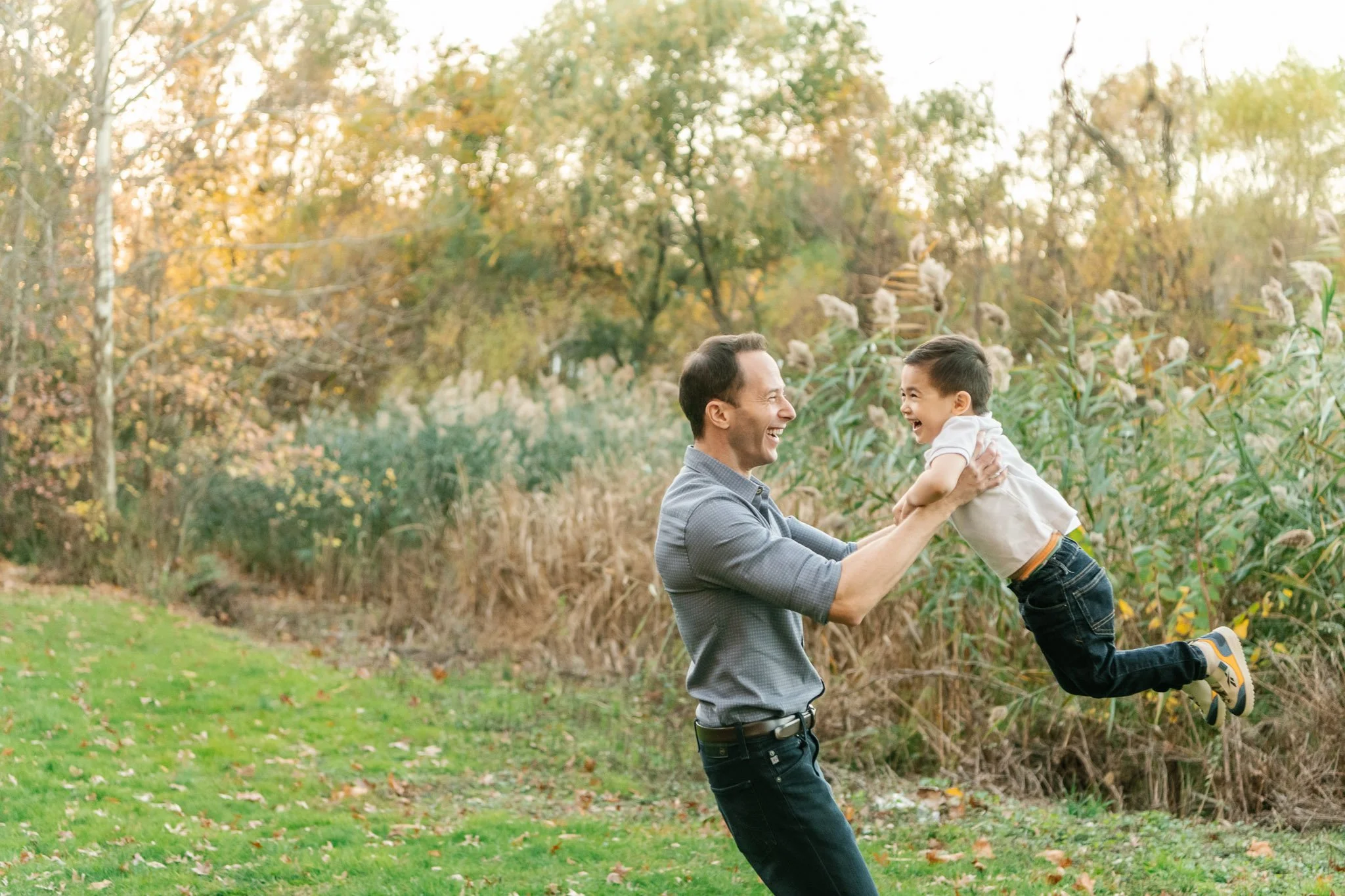  A father twirls his son around playing with him by Nicole Hawkins Photography. dad and lad playing together #NicoleHawkinsPhotography #NicoleHawkinsFamilies #fallfamilyphotos #NorthernNewJerseyPhotography #outdoorfamilyportraits 