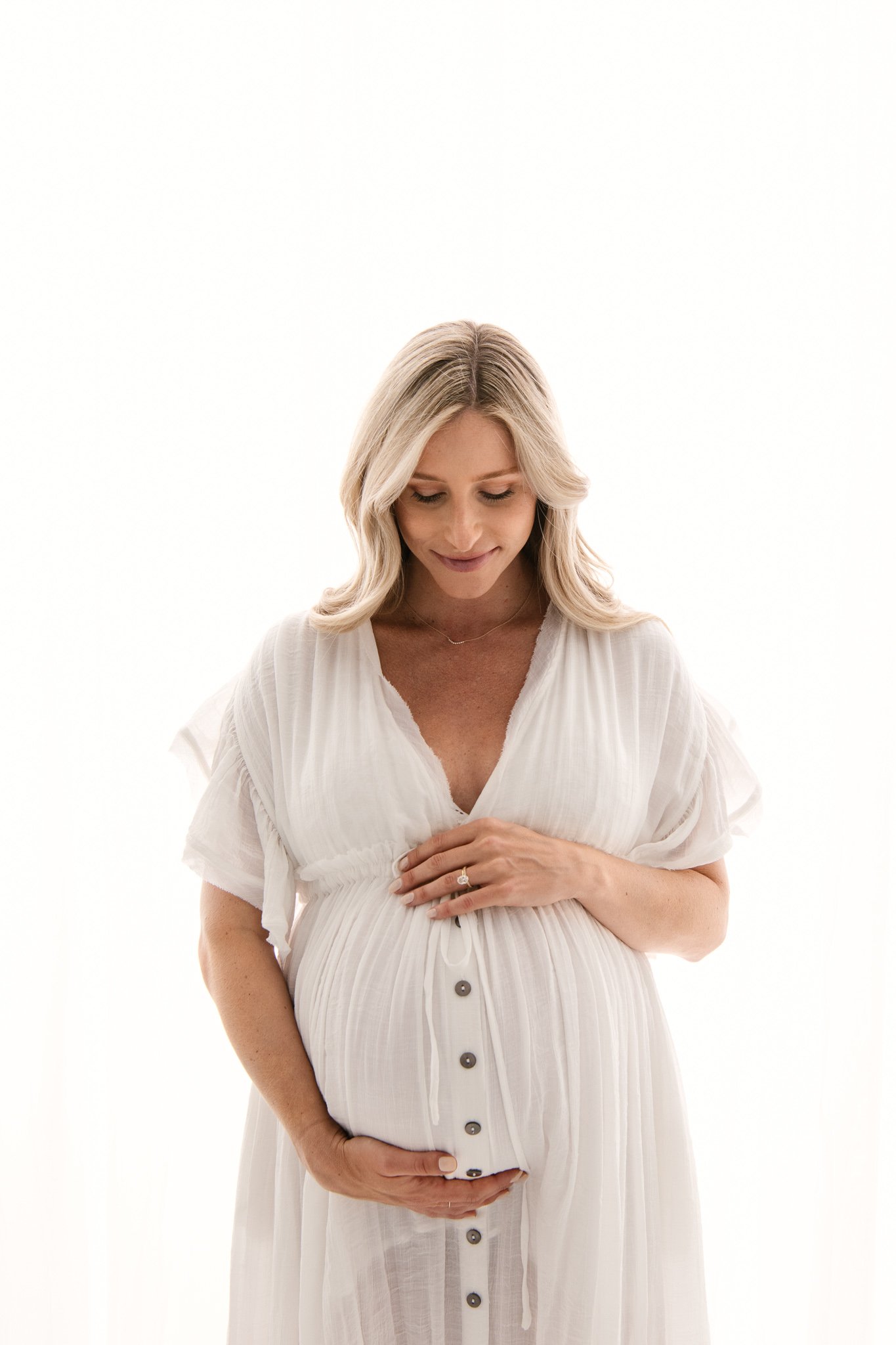  High-end studio photographer Nicole Hawkins Photography captures a woman with light featuring her face as she looks at her belly. baby #NicoleHawkinsPhotography #NicoleHawkinsMaternity #Studiomaternityportraits #NewJerseymaternity #NewYorkMaternity 