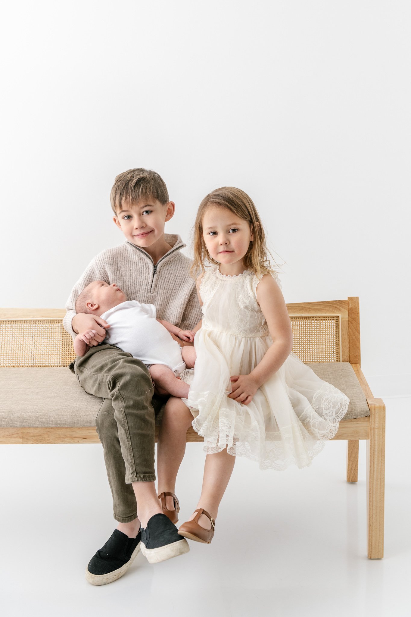  A brother and sister sit on a vintage bench holding their newborn baby sister by Nicole Hawkins Photography. vintage sibling portrait #NicoleHawkinsPhotography #NicoleHawkinsFamily #Newborns #MaplewoodNJ #studiofamilyportraits #modernfamilyportraits