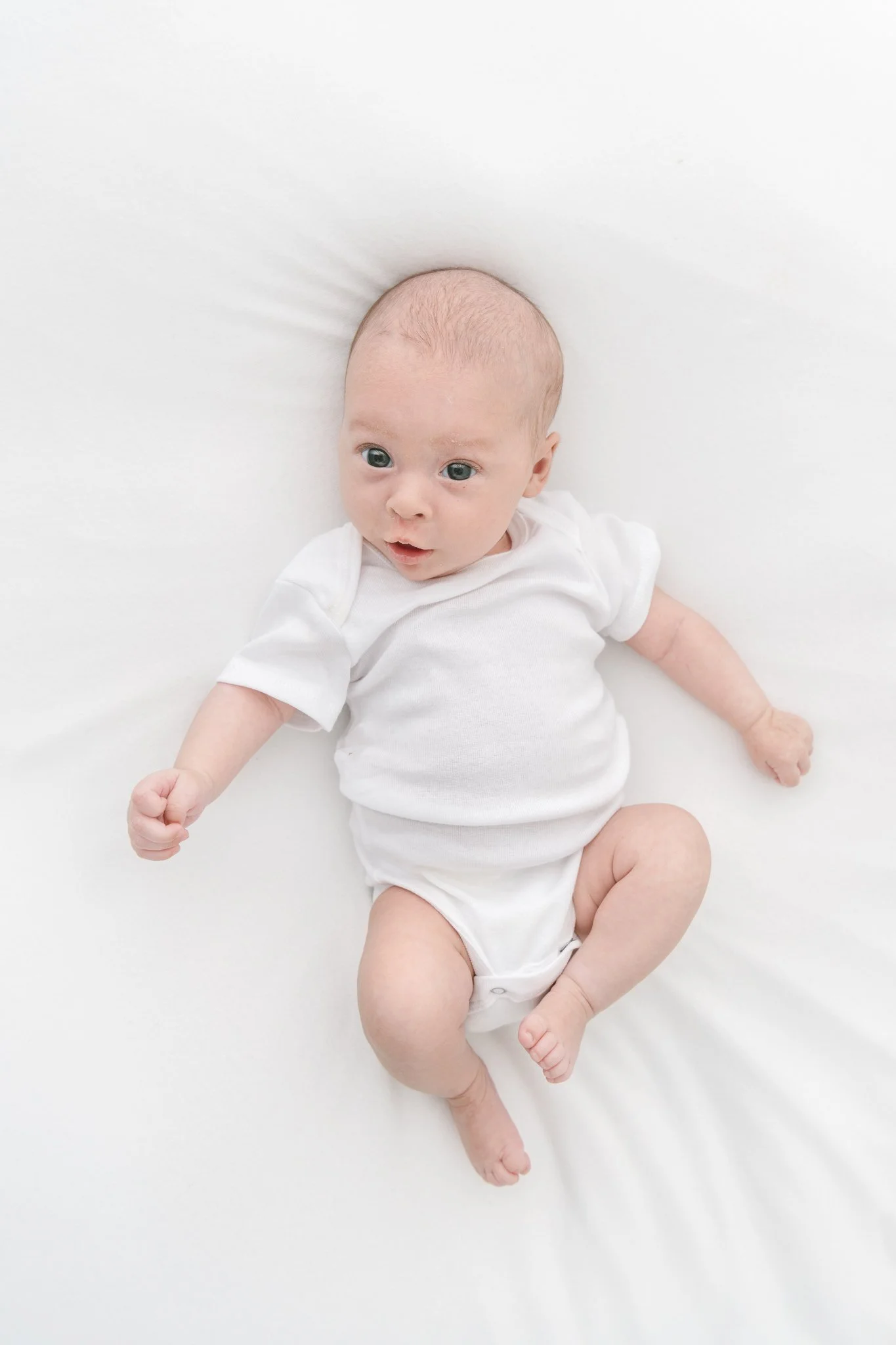  Studio newborn portrait in a white onesie with eyes wide open by Nicole Hawkins Photography. newborn pics eyes open #NicoleHawkinsPhotography #NicoleHawkinsFamily #Newborns #MaplewoodNJ #studiofamilyportraits #modernfamilyportraits 