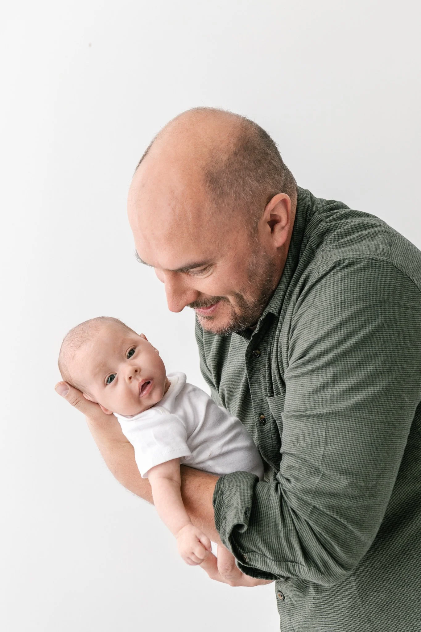  A father holds his newborn baby and smiles down at her captured by Nicole Hawkins Photography. father and baby studio #NicoleHawkinsPhotography #NicoleHawkinsFamily #Newborns #MaplewoodNJ #studiofamilyportraits #modernfamilyportraits 
