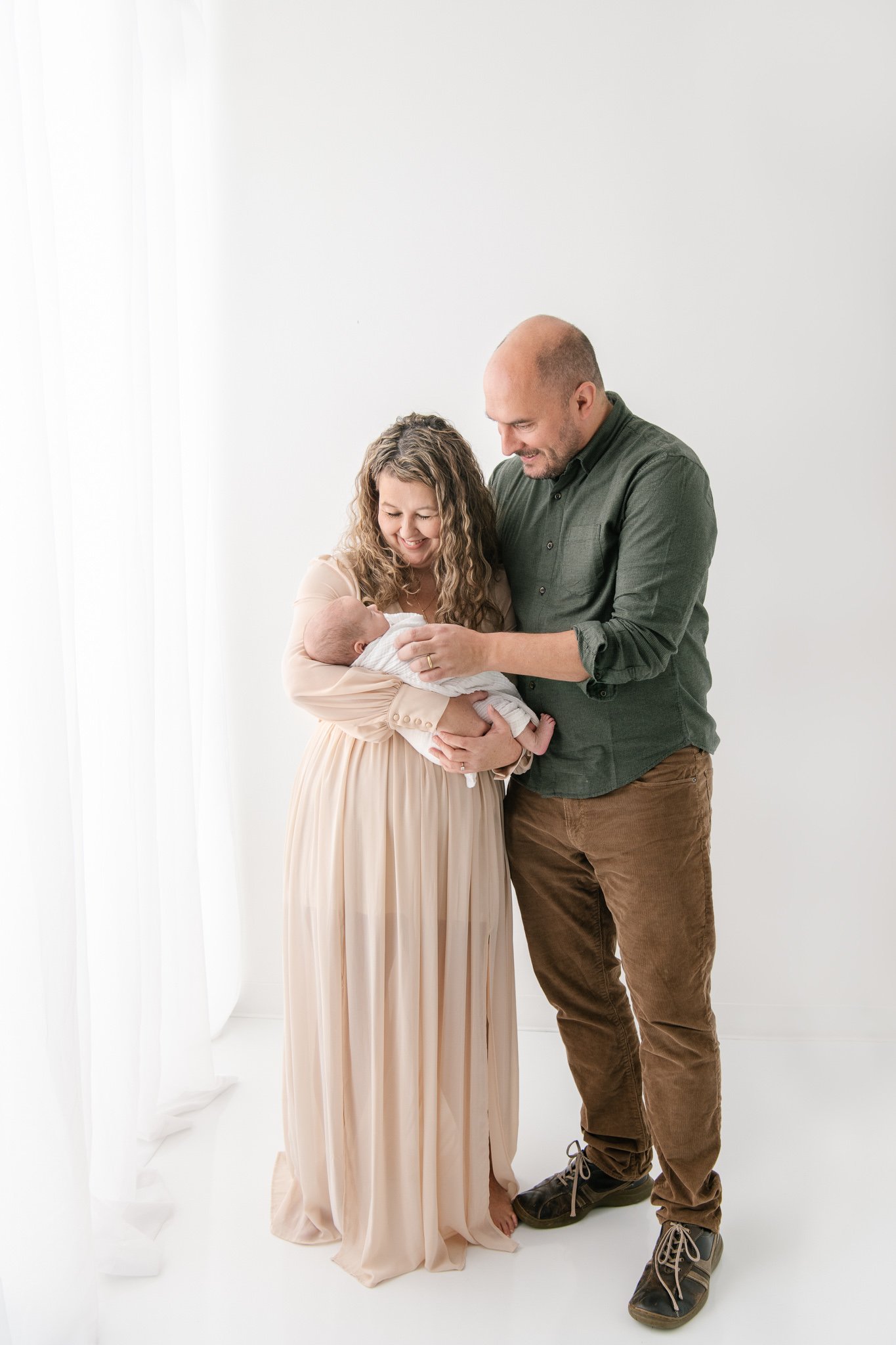  A father and mother look lovingly down at their newborn in a New Jersey studio family session with Nicole Hawkins Photography. three #NicoleHawkinsPhotography #NicoleHawkinsFamily #Newborns #MaplewoodNJ #studiofamilyportraits #modernfamilyportraits 