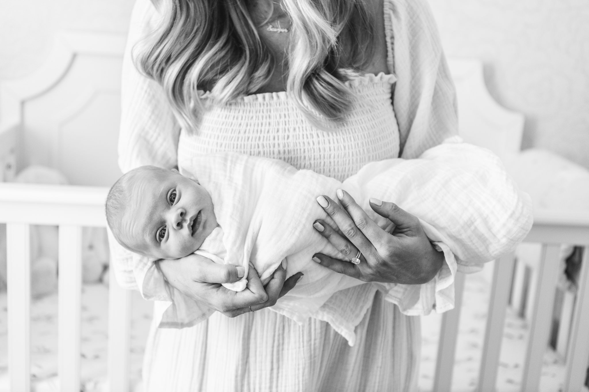  Newborn baby with eyes opened wide swaddled in a muslin blanket held by her mother by Nicole Hawkins Photography. eyes open newborn #NicoleHawkinsPhotography #NicoleHawkinsNewborns #InHomeNewborns #NewJerseyNewborns #NewYorkNewborns #babygirlnewborn