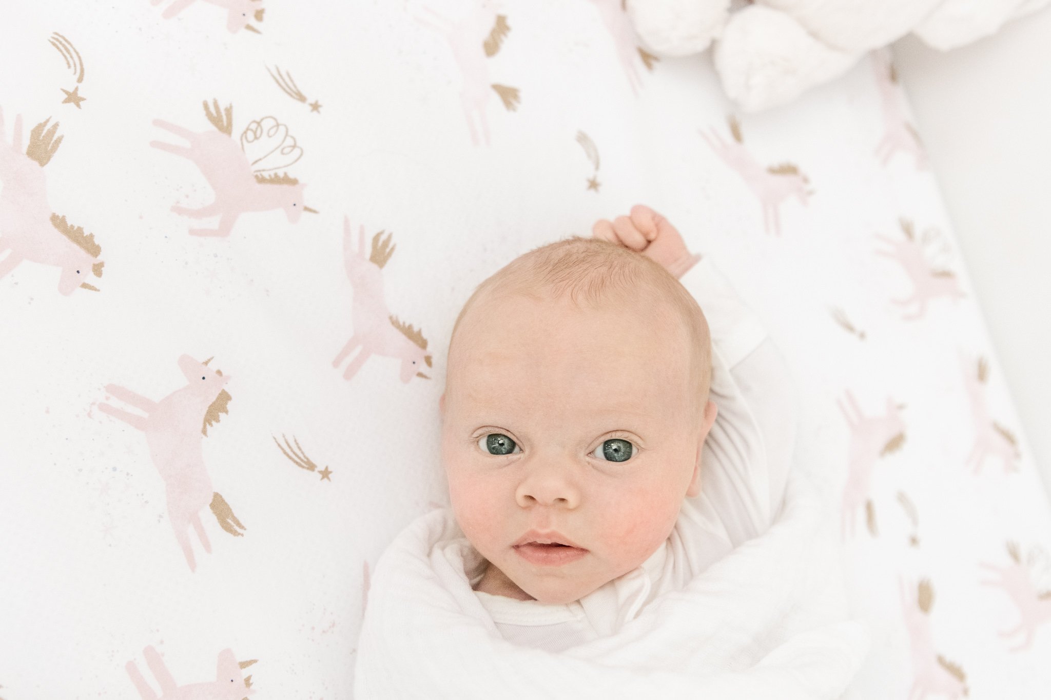  Nicole Hawkins Photography captures a baby girl lying in her crib with unicorn sheets. unicorn nursery eyes open #NicoleHawkinsPhotography #NicoleHawkinsNewborns #InHomeNewborns #NewJerseyNewborns #NewYorkNewborns #babygirlnewborns 