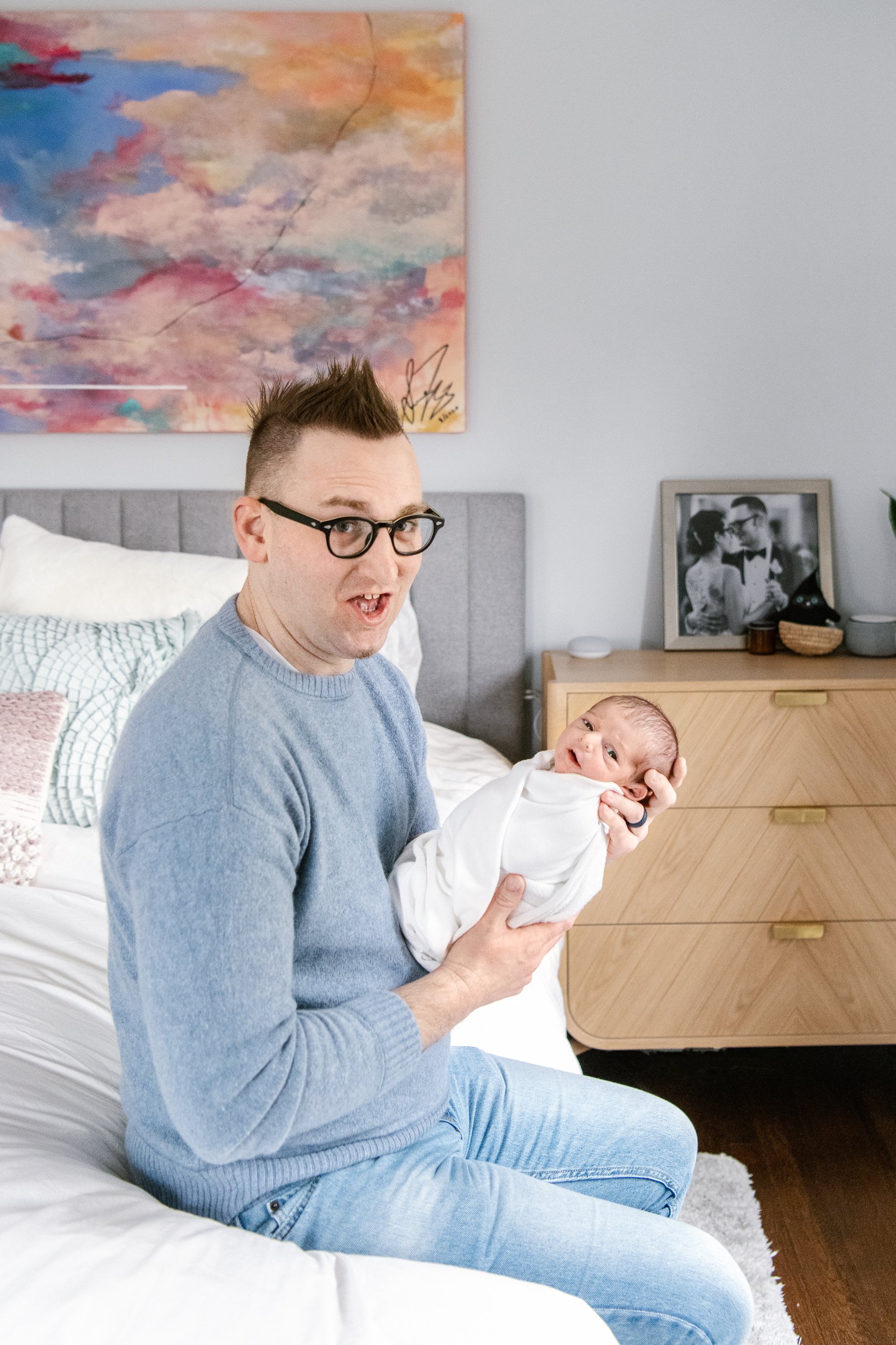  New Jersey newborn photographer captures a dad making a silly face sitting on a bed with his baby girl. father and baby #NicoleHawkinsPhotography #NicoleHawkinsFamily #Newborns #InHomeNewborns #NicoleHawkinsNewborns #NJnewborns #babygirl 