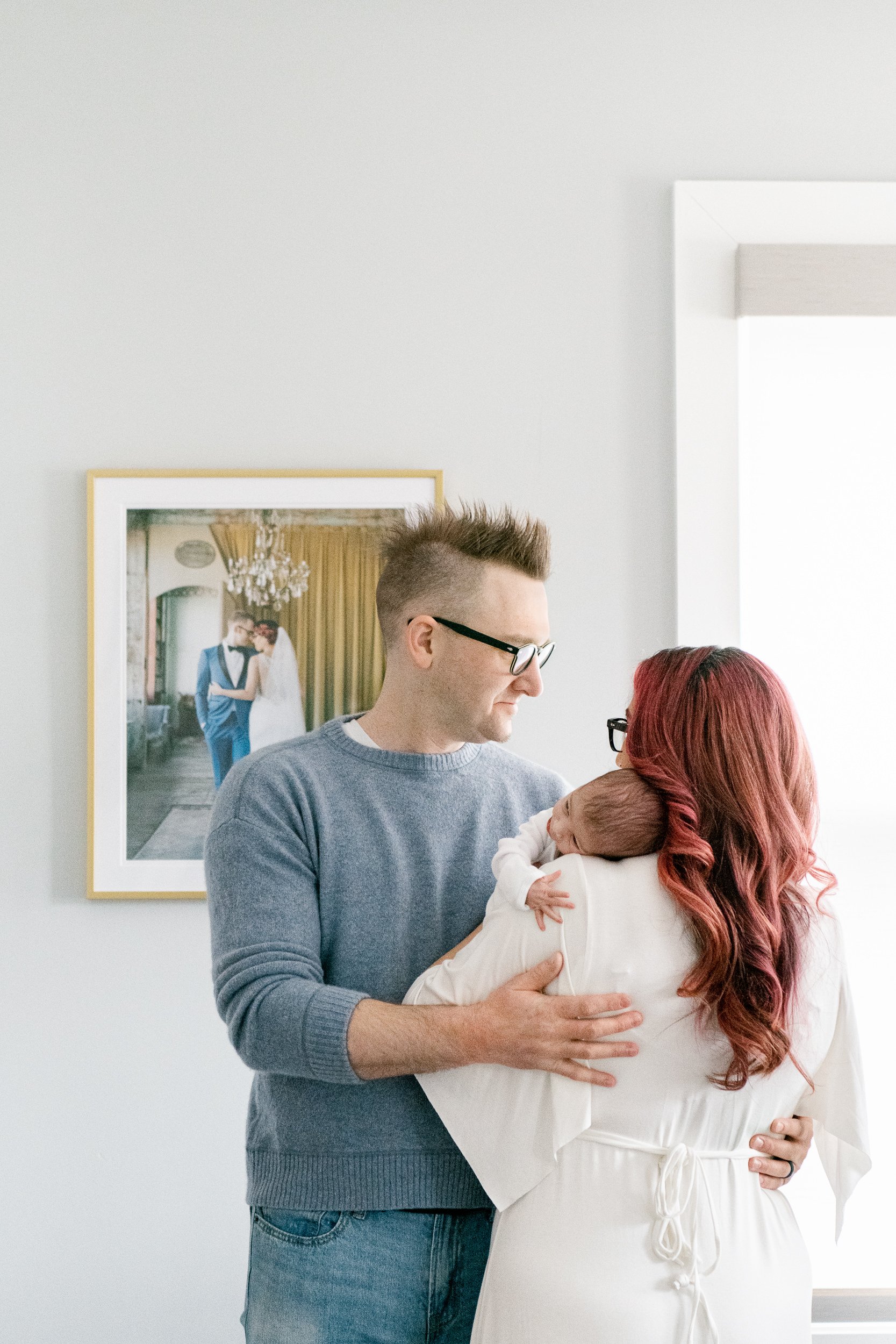  Portrait of new parents and baby standing next to wedding portrait by Nicole Hawkins Photography. time change portrait #NicoleHawkinsPhotography #NicoleHawkinsFamily #Newborns #InHomeNewborns #NicoleHawkinsNewborns #NJnewborns #babygirl 