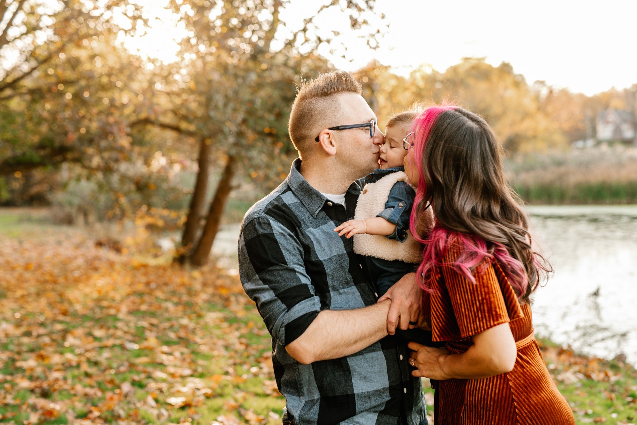  Mother and father kiss their toddler on the face during family pictures with Nicole Hawkins Photography. family poses #NicoleHawkinsPhotography #NicoleHawkinsFamily #fallfamilyphotos #fallphotos #familyphotographerNJ #NJfallfamilypics 