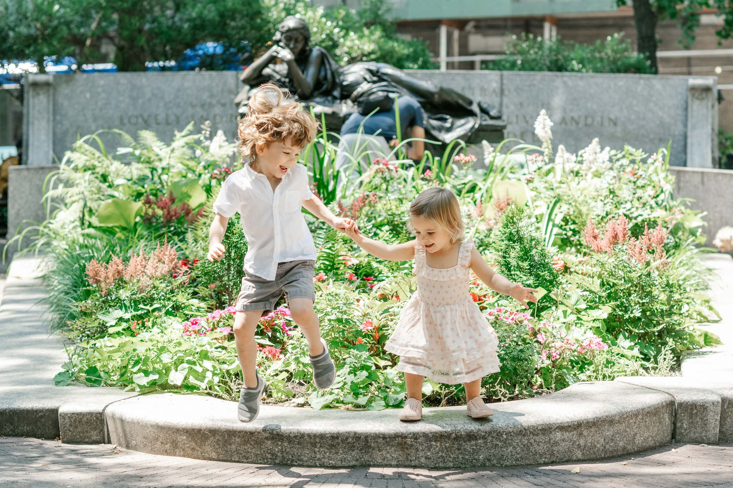  Nicole Hawkins Photography captures a boy and girl jumping off a flower bed holding hands. NYC photography #NicoleHawkinsPhotograaphy #NicoleHawkinsChildren #NewYorkPortraits #KidsinNewYork #ChildrensPortraits #lifestyleportraits 
