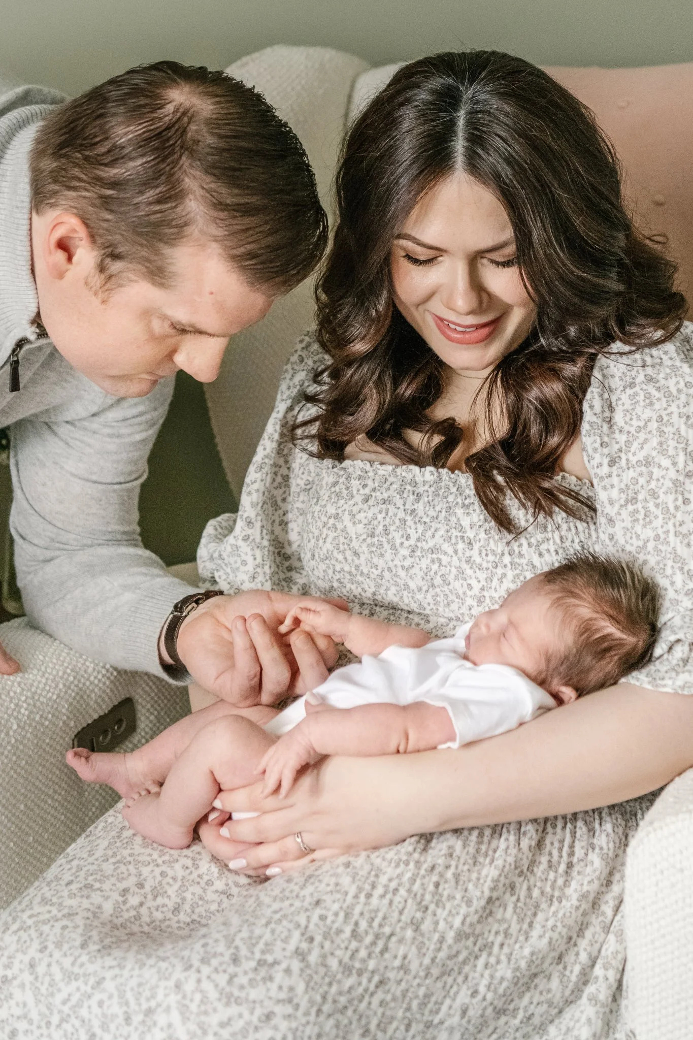  As a mother holds a baby a father holds the baby's hand by Nicole Hawkins Photography. mother father and baby at home in Montclair, New Jersey #NicoleHawkinsPhotography #NicoleHawkinsNewborns #MontclairNewbornPhotographer #InHomeNewborns #NJNewborns