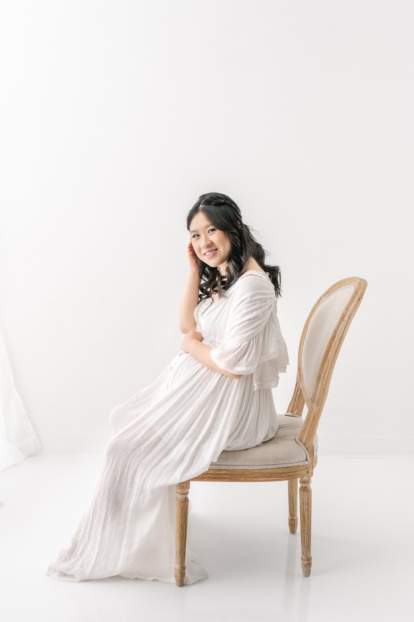  Soon-to-be mother sitting on a chair in a white studio by Nicole Hawkins photography in New Jersey. new jersey maternity photography #NicoleHawkinsPhotography #NicoleHawkinsMaternity #MaternityPhotography #Maternitystyle #NJMaternity #TimelessPortra