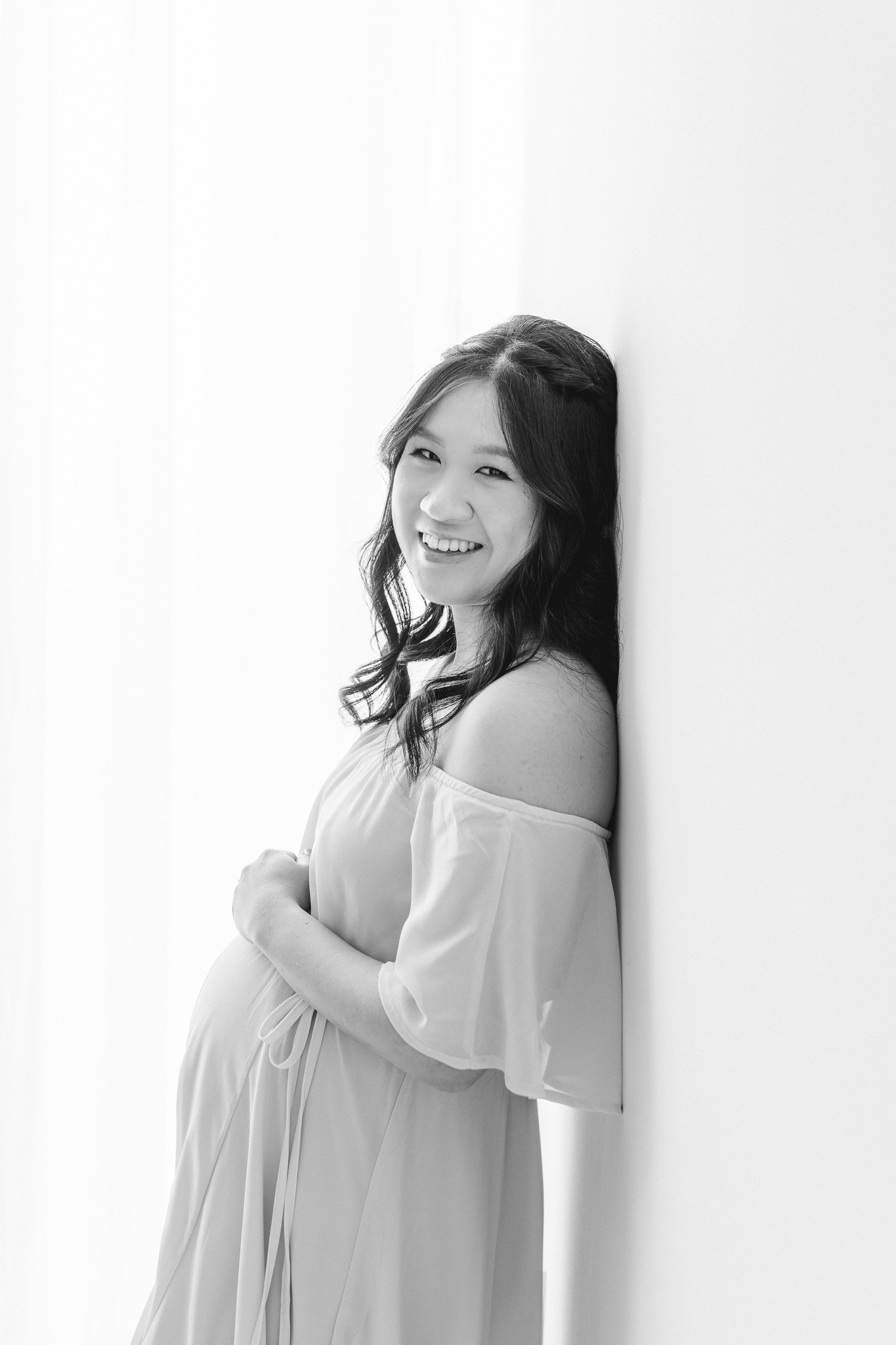  Nicole Hawkins Photography captures a glowing mother holding her belly and leaning against a wall. glowing maternity shot black and white #NicoleHawkinsPhotography #NicoleHawkinsMaternity #MaternityPhotography #Maternitystyle #NJMaternity #TimelessP