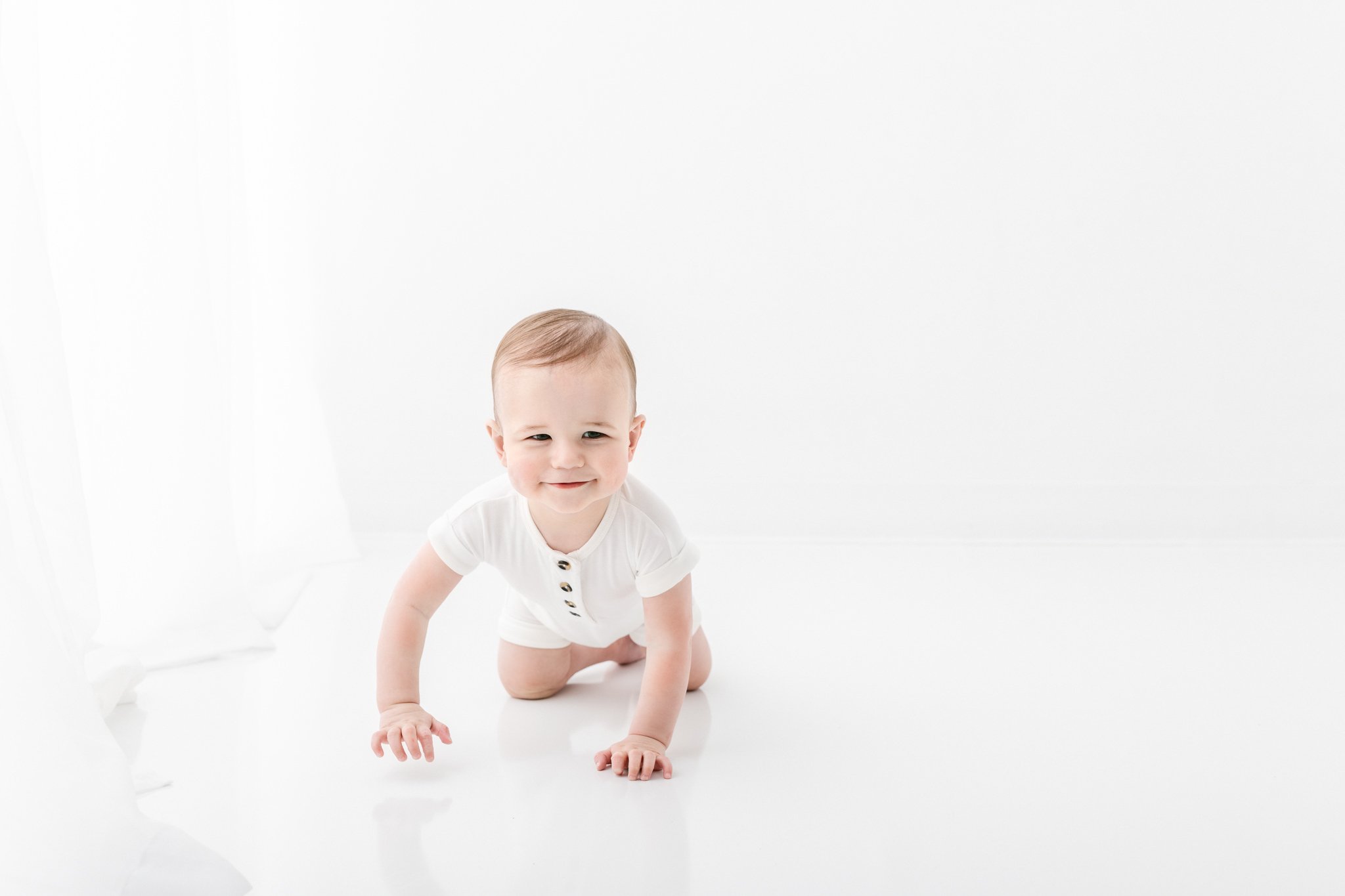  White studio portrait of a one-year-old baby boy by Nicole Hawkins Photography. white outfits for baby boy boy crawling #NicoleHawkinsPhotography #NicoleHawkinsBabies #FirstBirthdayPhotography #StudioFamilyPortraits #NJBabies #FirstBirthday #StudioB