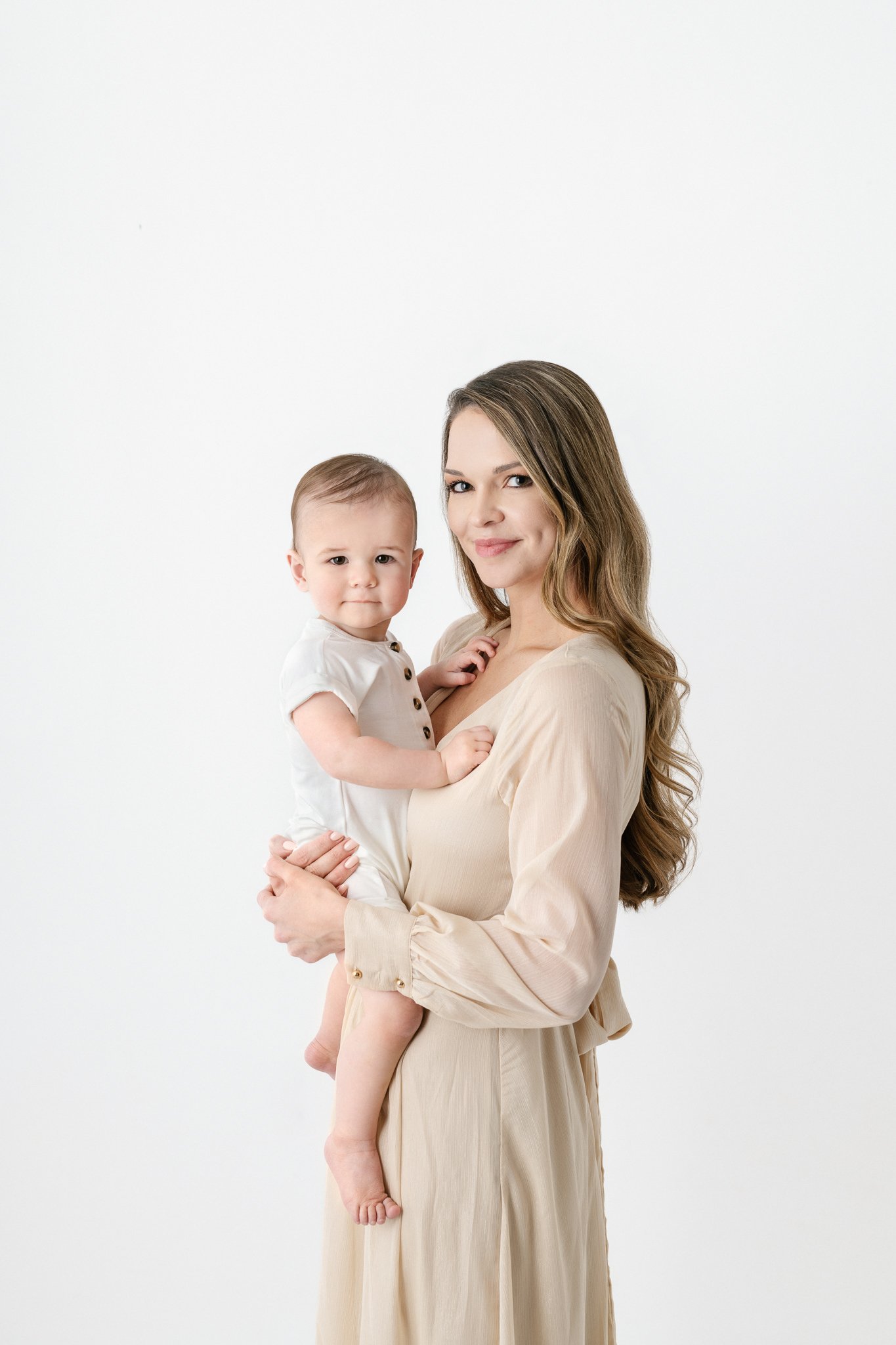  Portrait of a mother holding her baby boy in an all-white studio by Nicole Hawkins Photography. mother and baby studio portrait #NicoleHawkinsPhotography #NicoleHawkinsBabies #FirstBirthdayPhotography #StudioFamilyPortraits #NJBabies #FirstBirthday 