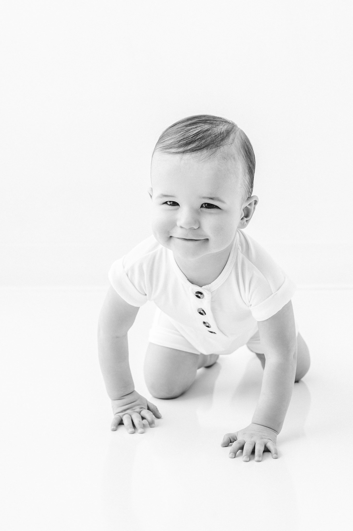  Baby boy crawling around in a white studio in New Jersey by Nicole Hawkins Photography. smiling crawling one year old baby birthday portraits #NicoleHawkinsPhotography #NicoleHawkinsBabies #FirstBirthdayPhotography #StudioFamilyPortraits #NJBabies #