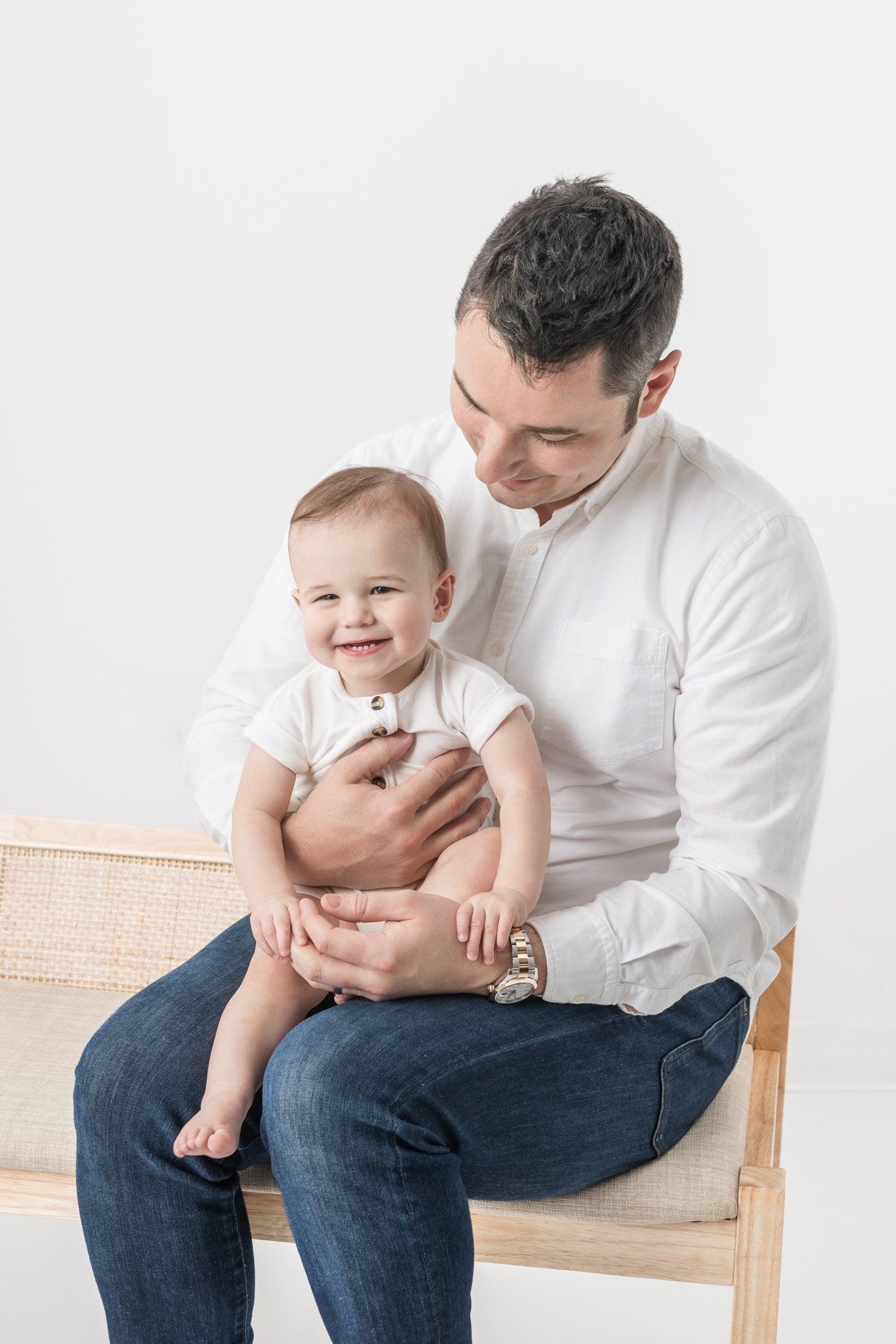  Toddler boy laughs while sitting with his daddy at a Studio in New Jersey by Nicole Hawkins Photography. father with baby studio modern family portraits #NicoleHawkinsPhotography #NicoleHawkinsBabies #FirstBirthdayPhotography #StudioFamilyPortraits 