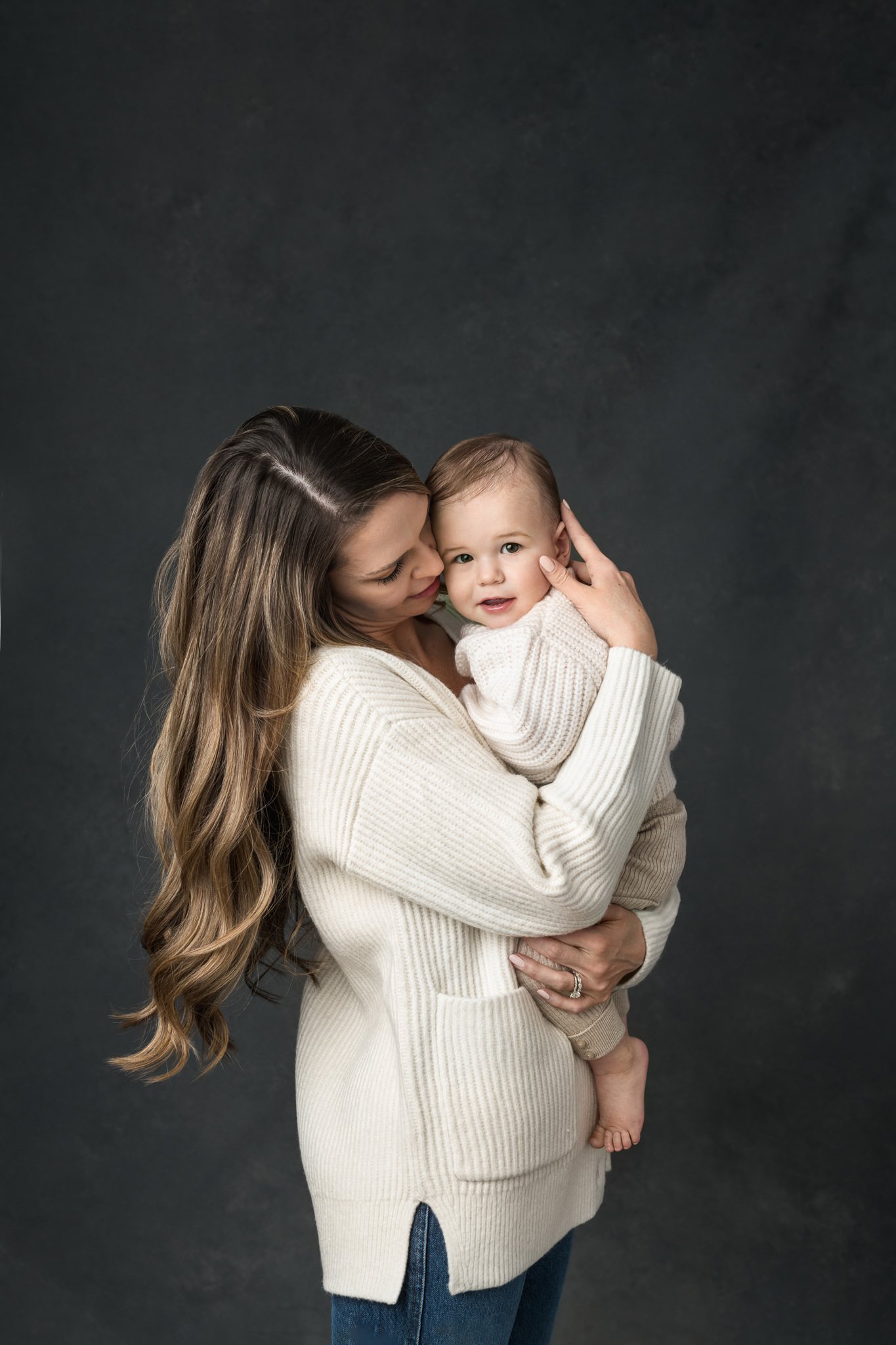  A mother holds her baby boy in her arms kissing him during his first birthday photoshoot with Nicole Hawkins PHotography. mother kisses her baby boy one year old #NicoleHawkinsPhotography #NicoleHawkinsBabies #FirstBirthdayPhotography #StudioFamilyP